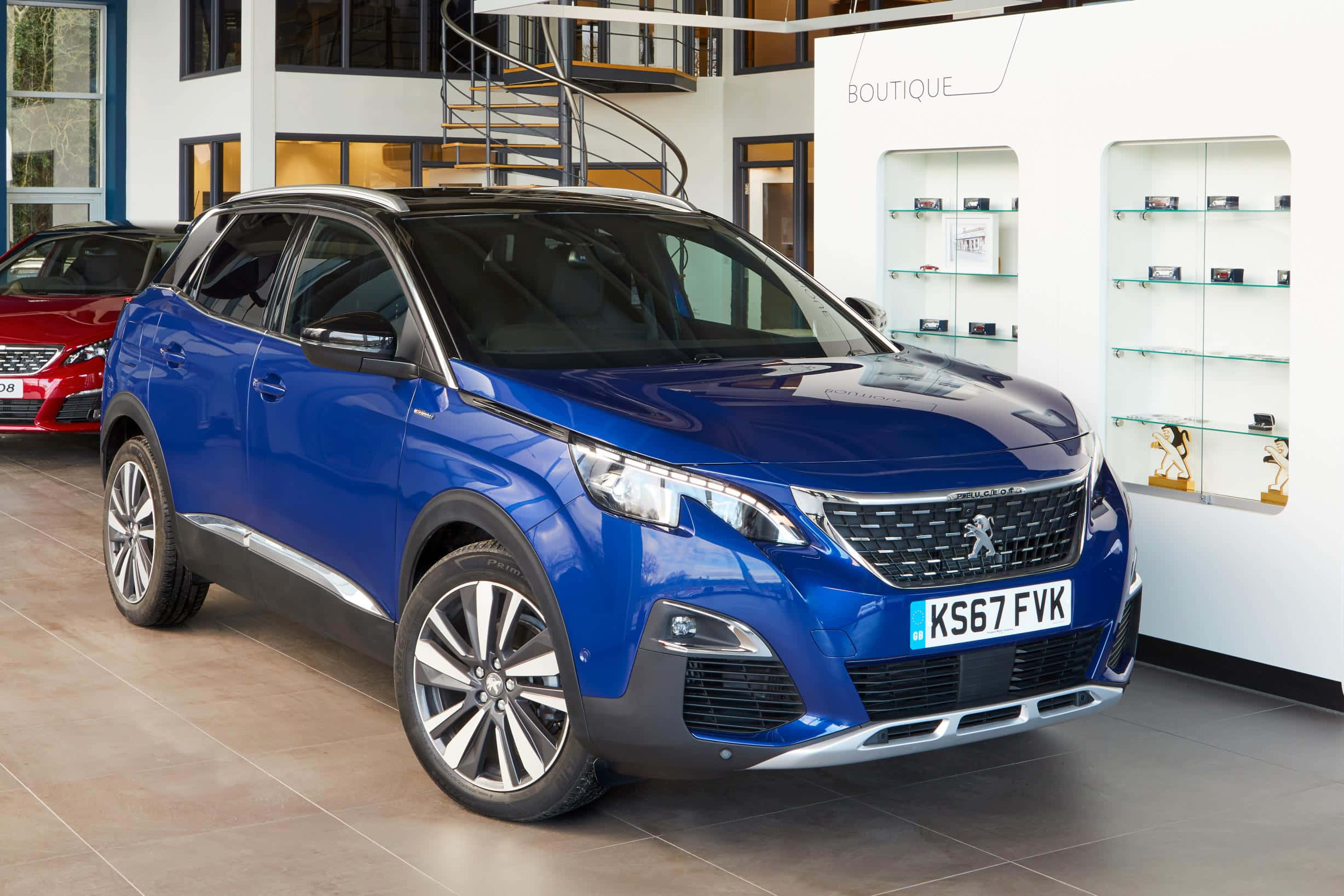 Peugeot 5008 桌布 壁紙 — 一輛光澤藍色Peugeot SUV在現代汽車經銷商中展示，地板鋪有瓷磚，玻璃架上陳列著商品。