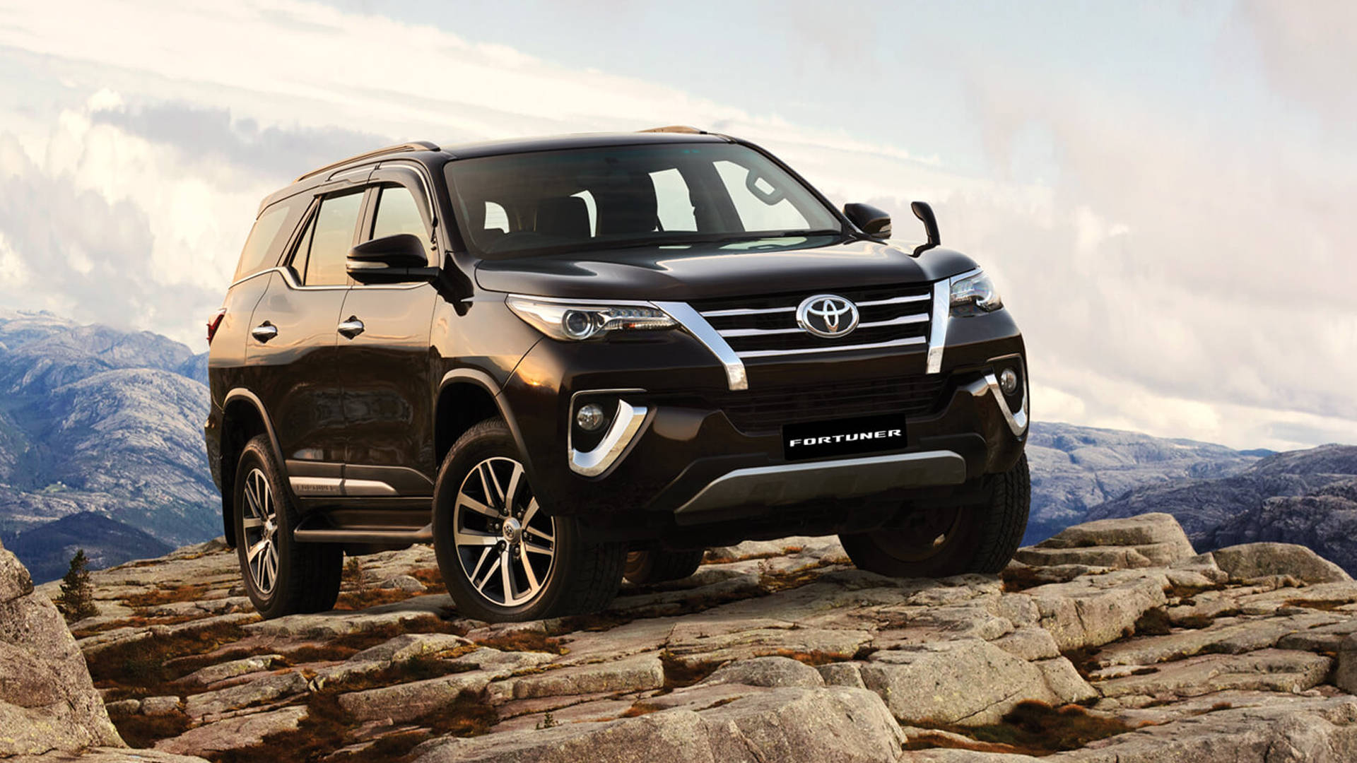 黑色豐田 Fortuner SUV 在岩石山地地形上，背景有山脈。 — Toyota Supra 壁紙