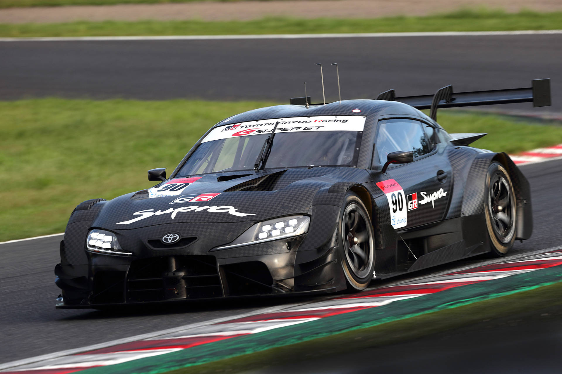黑色豐田Supra賽車在紅白綠三色路緣的賽道上飛馳。 — Toyota Supra 壁紙