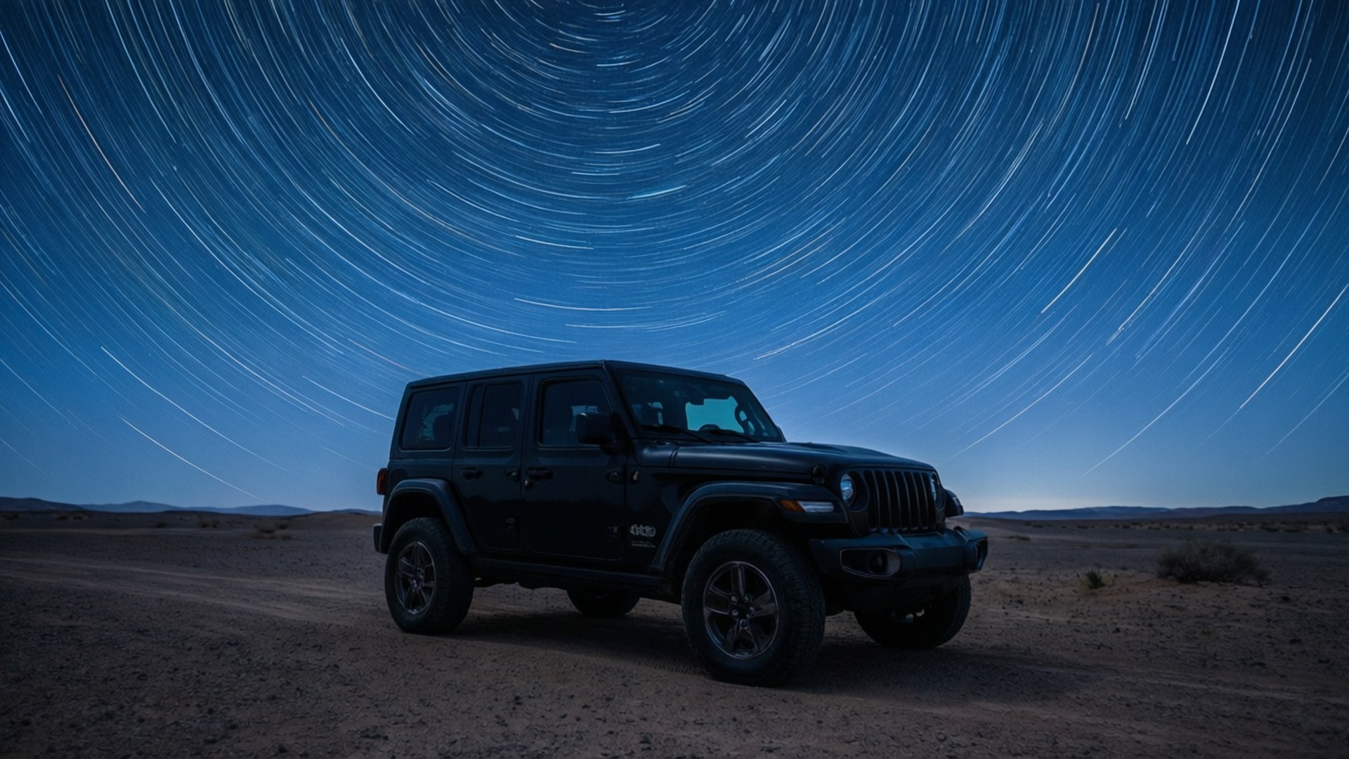 Desert Night Stars 壁紙 — 一輛黑色Jeep Wrangler停在沙漠公路上，上方是帶有旋轉星軌的鮮豔藍天。