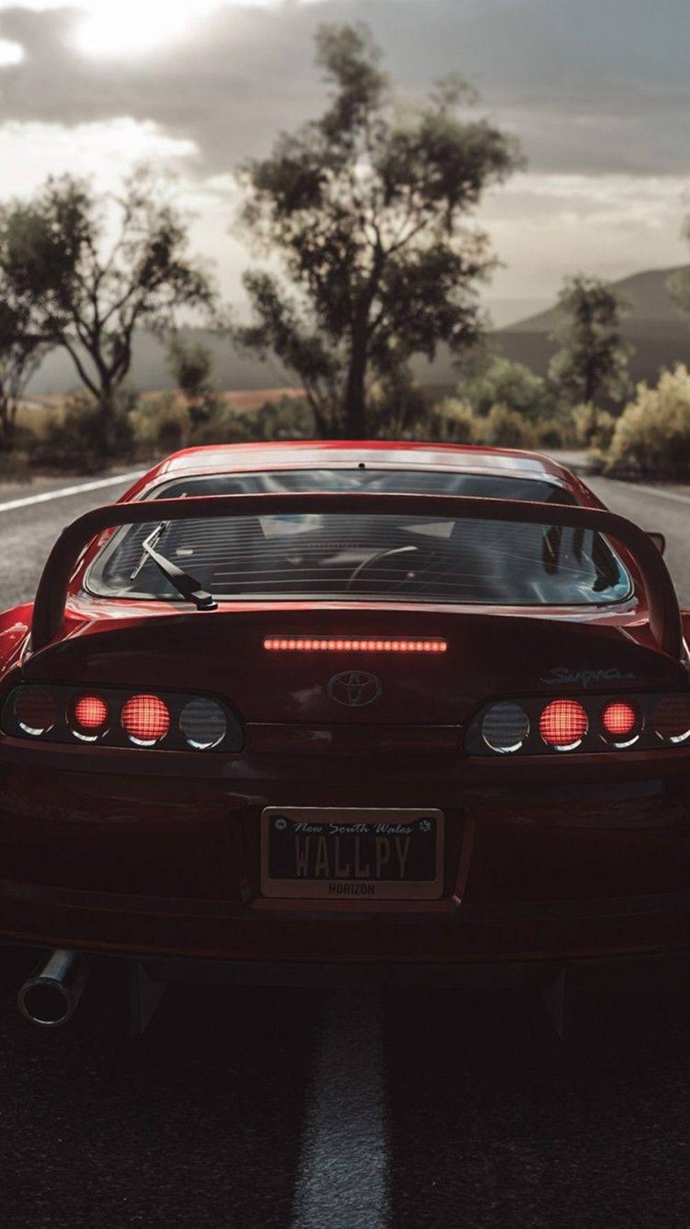 紅色跑車在黃昏時分行駛在山路上，尾燈發光。 — Toyota Supra 壁紙