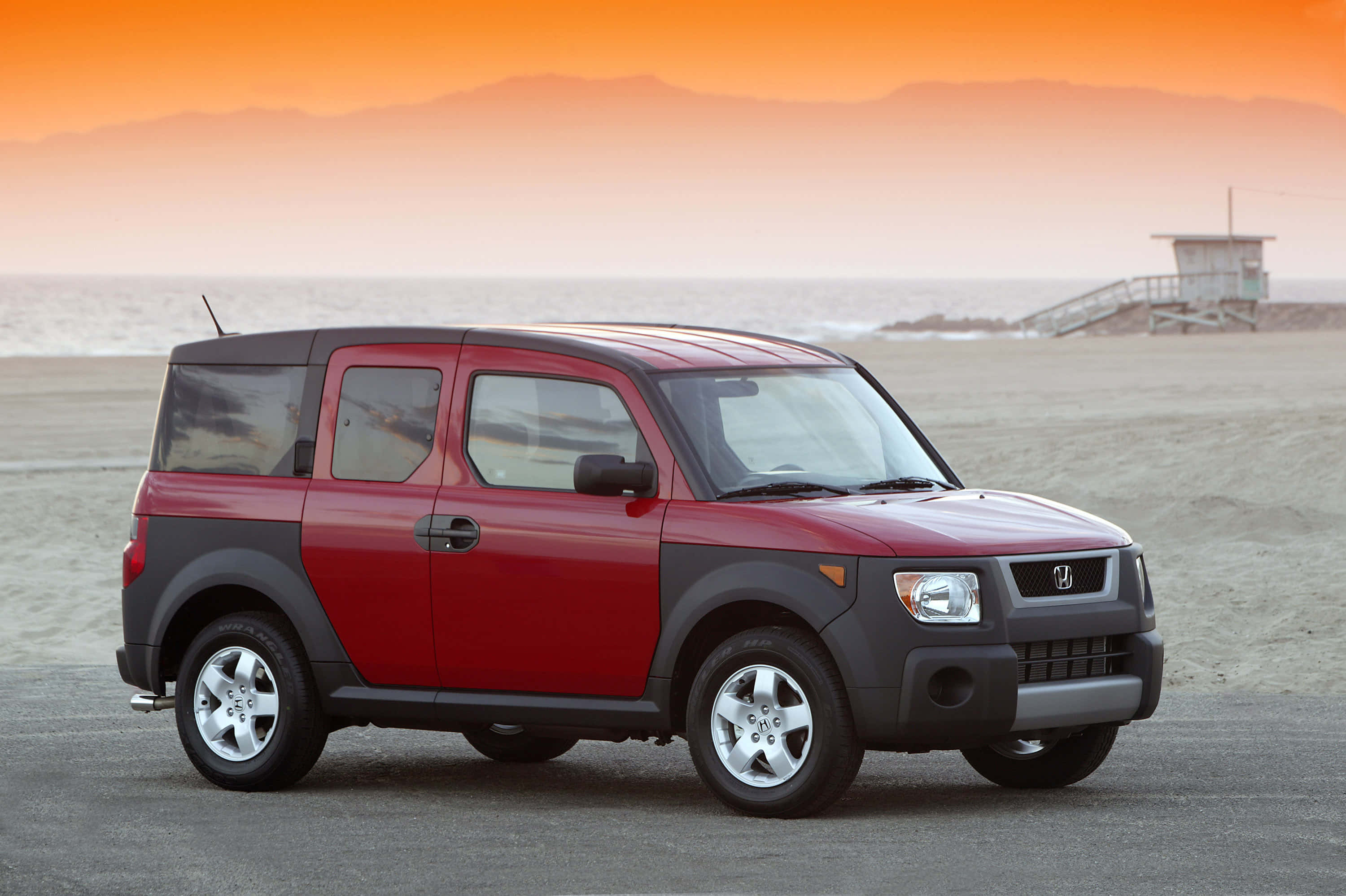 Honda Element 桌布 壁紙 — 一輛紅色和黑色的本田Element停泊在日落時分的沙灘上，背景有山脈和救生塔。