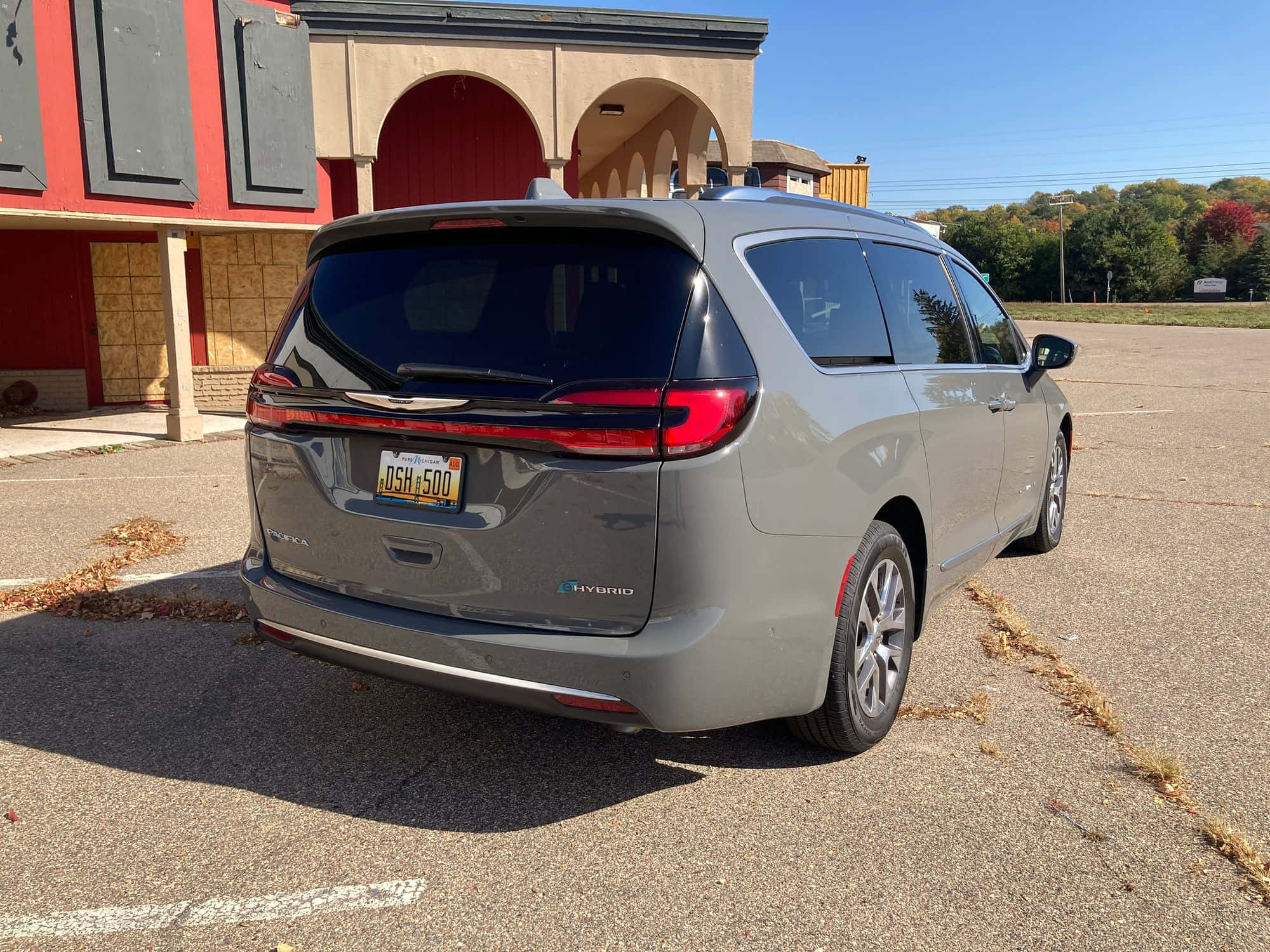 Chrysler Pacifica 桌布 壁紙 — 一輛灰色克萊斯勒Pacifica Hybrid迷你廂型車停放在停車場，有秋葉，在明亮的日光下。