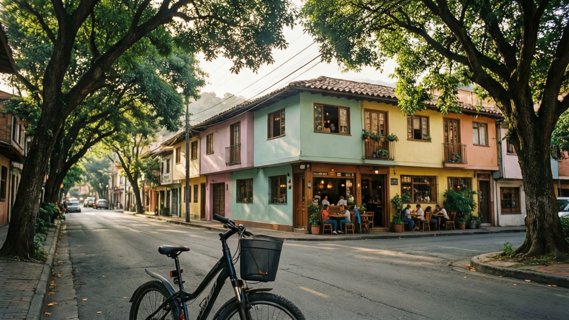 Laureles Neighborhood Charm 壁紙 — 一輛腳踏車停放在綠樹成蔭的街道上，旁邊是粉彩色的建築物，人們在戶外咖啡桌用餐。
