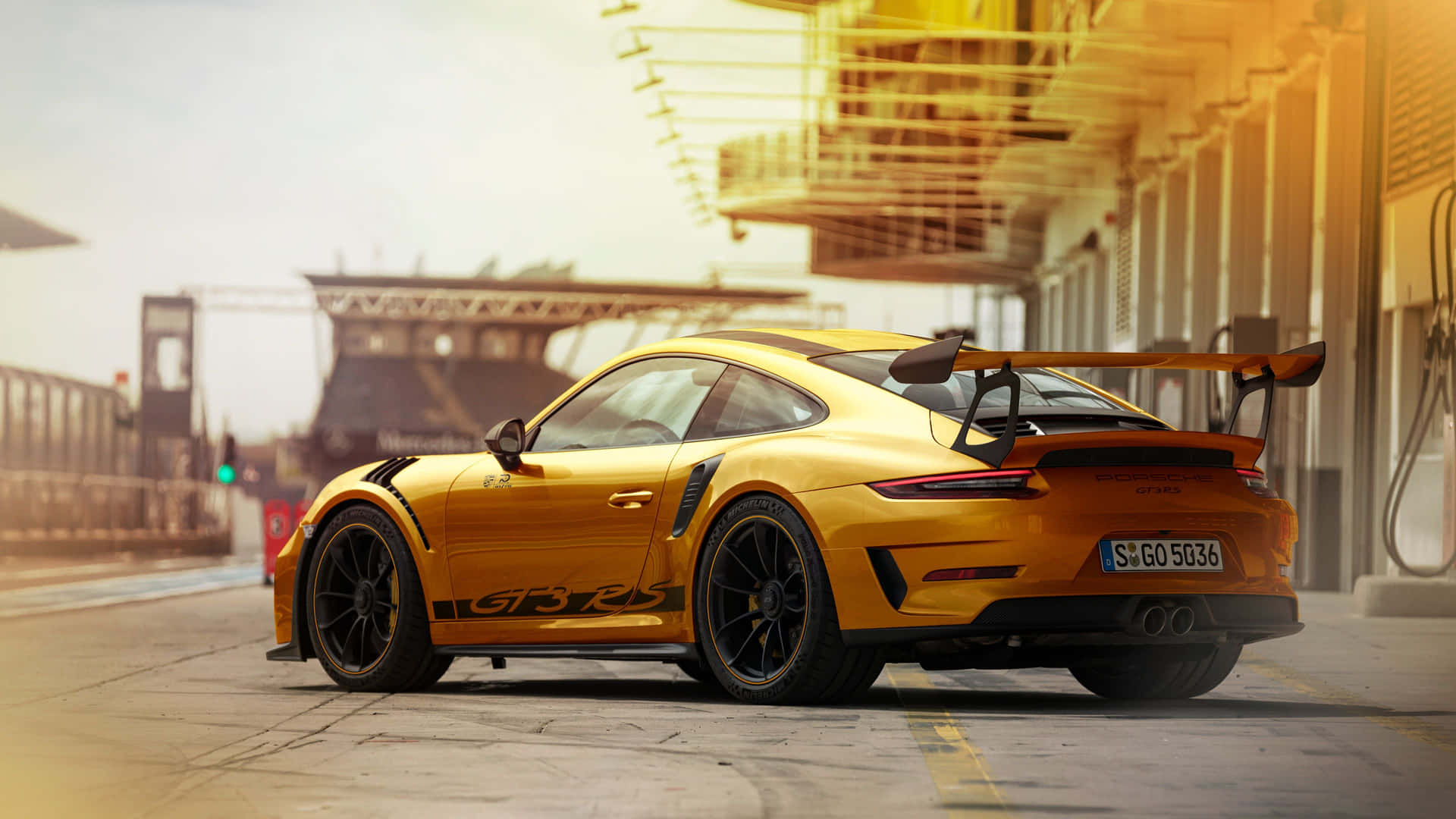  壁紙 — 一輛金色保時捷911 GT3 RS跑車停放在賽車場車庫，沐浴在溫暖的金色光線下。