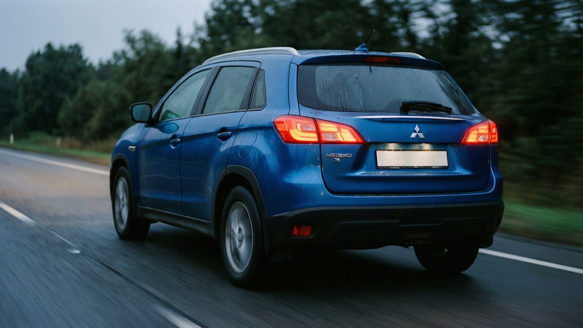 Mitsubishi Asx 桌布 壁紙 — 一輛藍色三菱ASX SUV在黃昏時分行駛在濕滑的道路上，背景是模糊的樹木。