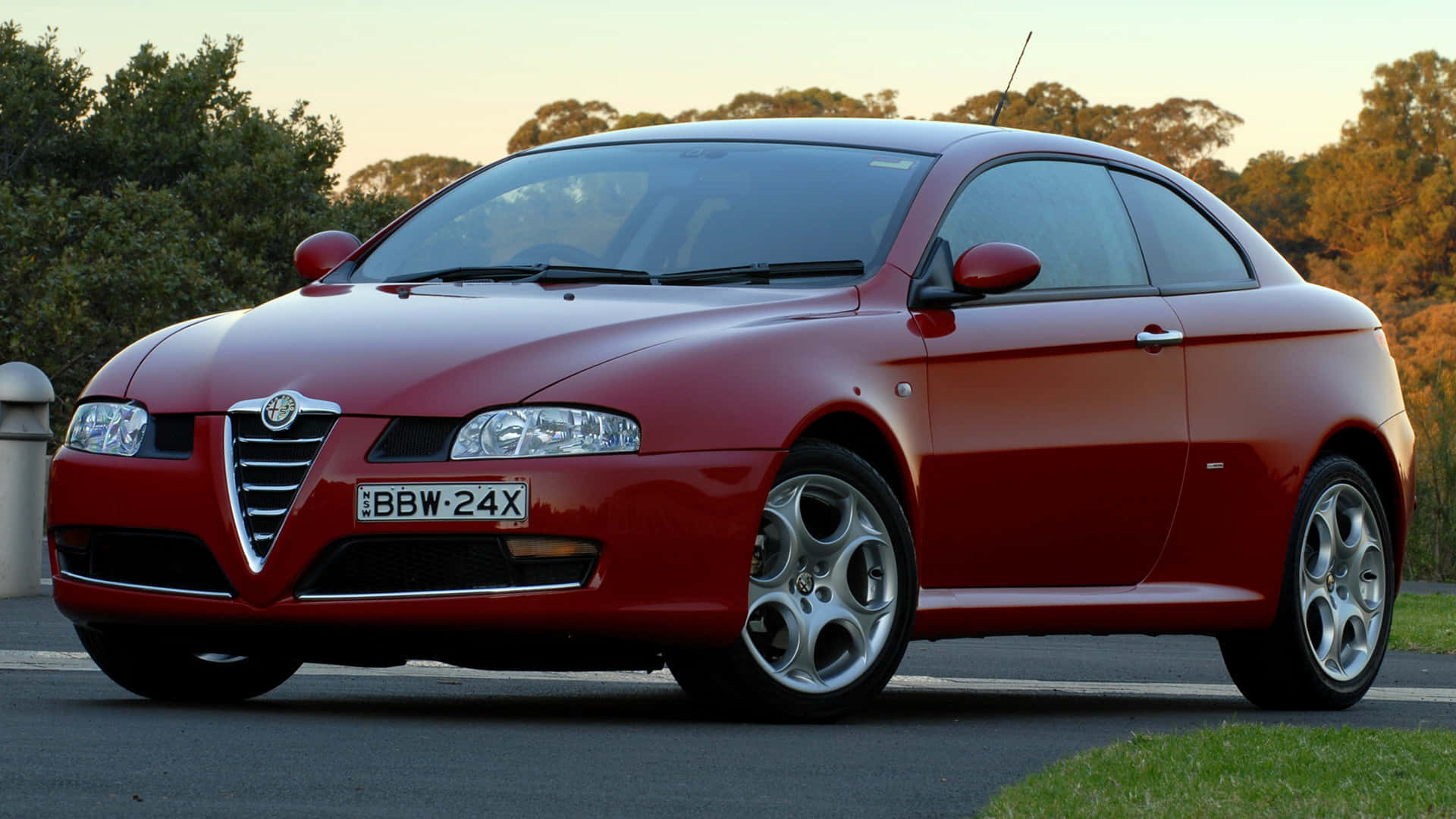 Alfa Romeo Gt 桌布 壁紙 — 一輛亮紅色的Alfa Romeo雙門跑車在黃金時段停泊在路邊，背景有樹木。