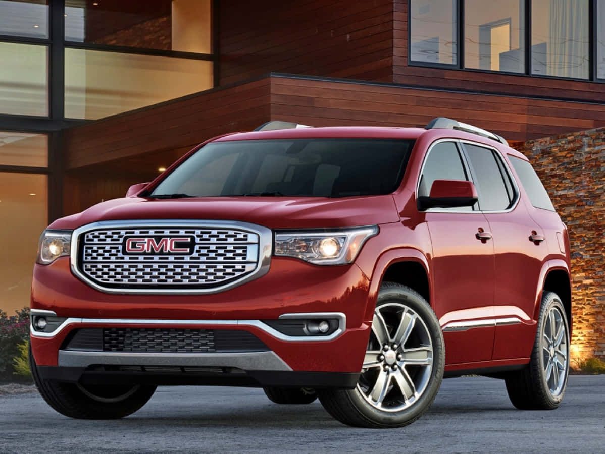 Gmc Acadia 桌布 壁紙 — 一輛亮紅色的GMC Acadia SUV停在一間帶有溫暖照明的現代木屋前。