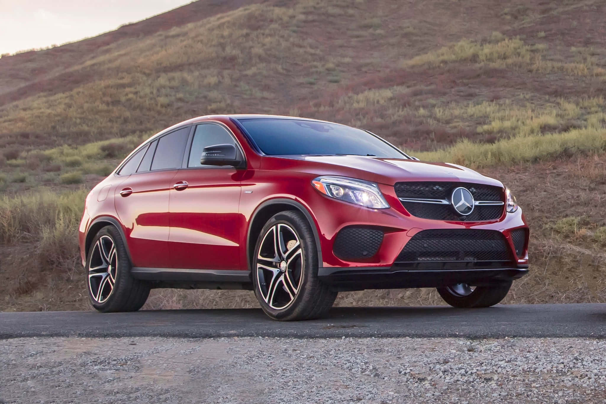 Mercedes Benz Gle-class 桌布 壁紙 — 一輛亮紅色的梅賽德斯 GLE 轎跑車停在碎石路上，背景是乾燥的草坡，正值黃金時刻。
