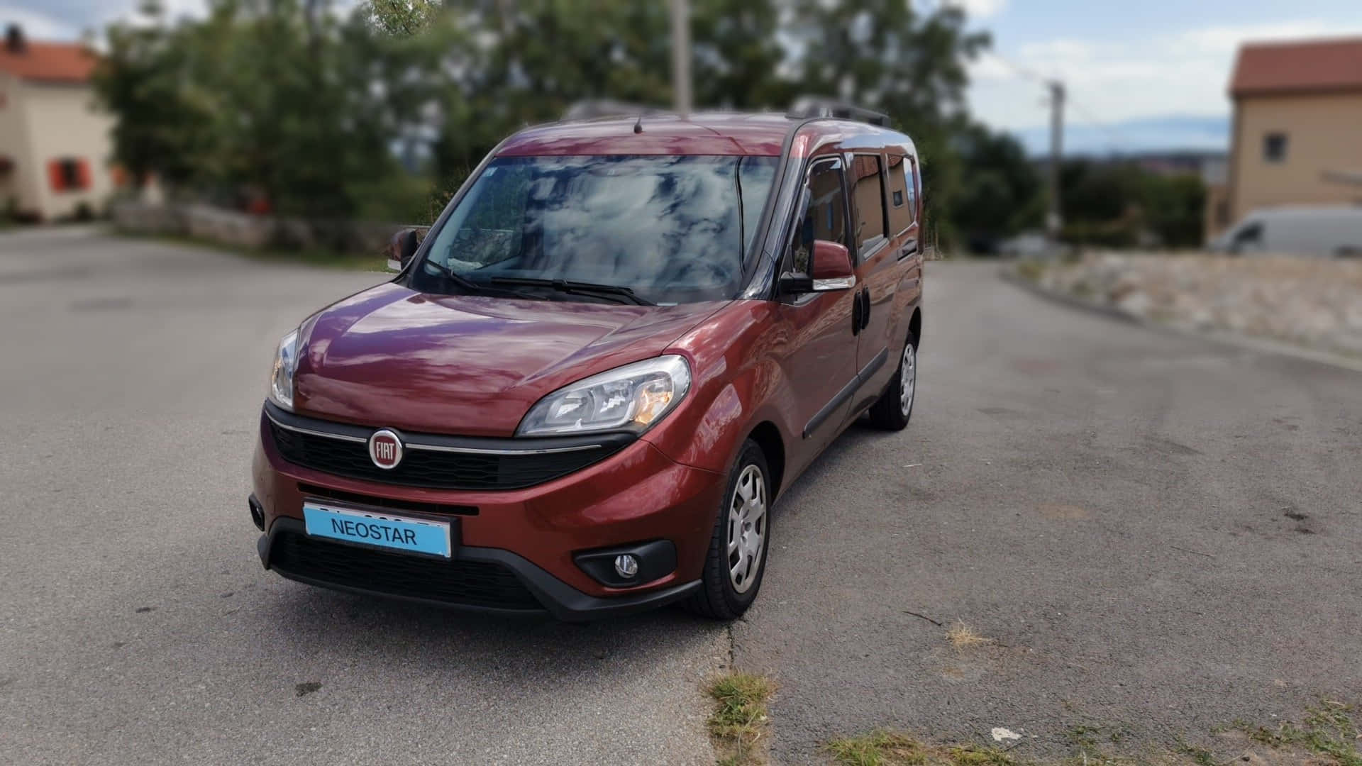  壁紙 — 一輛亮紅色的 Fiat Neostar 廂型車停放在寧靜的柏油路上，背景有樹木和房屋。