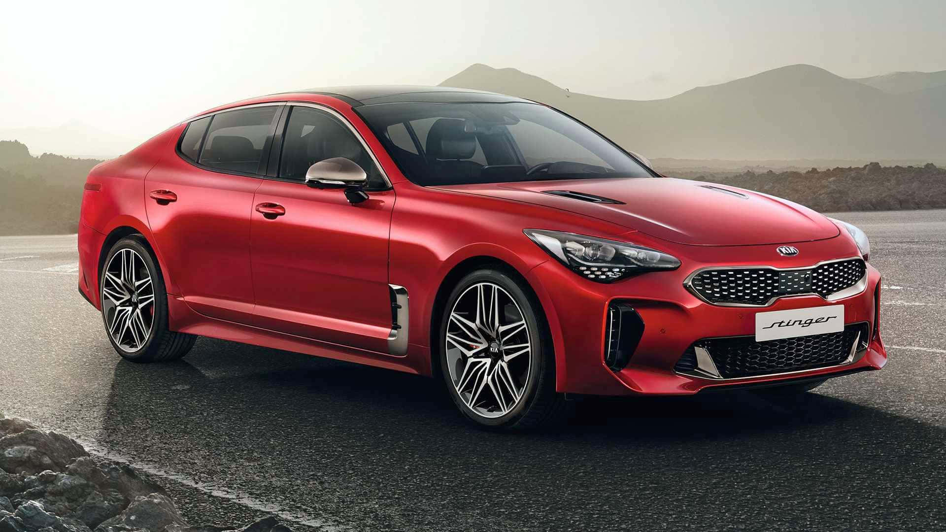 Kia Stinger 桌布 壁紙 — 一輛亮紅色Kia Stinger運動轎車停在濕漉漉的瀝青路上，背景有朦朧的山巒。