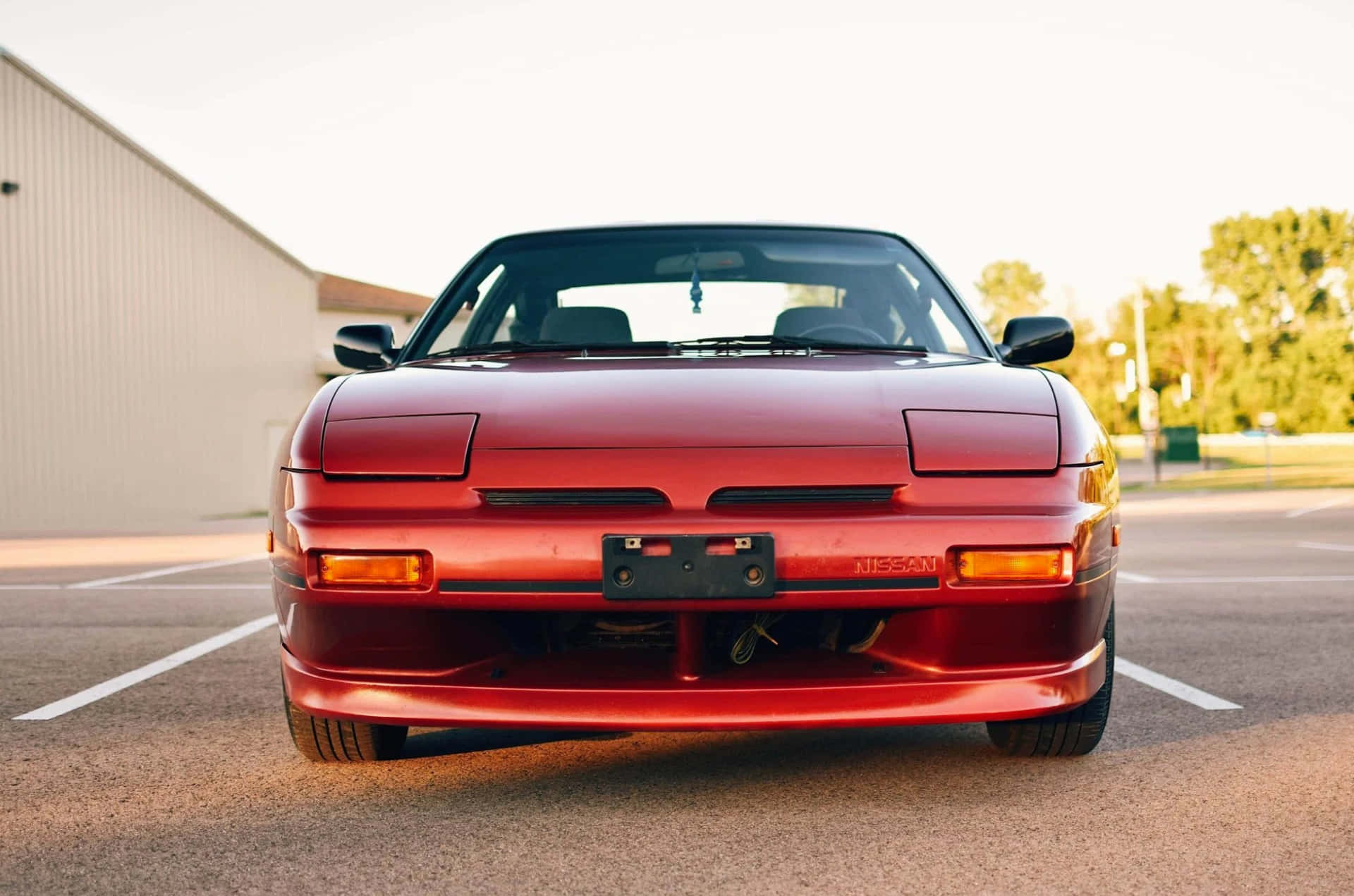 壁紙 — 一輛亮紅色日產240SX跑車停放在停車場，帶有溫暖的日落燈光。