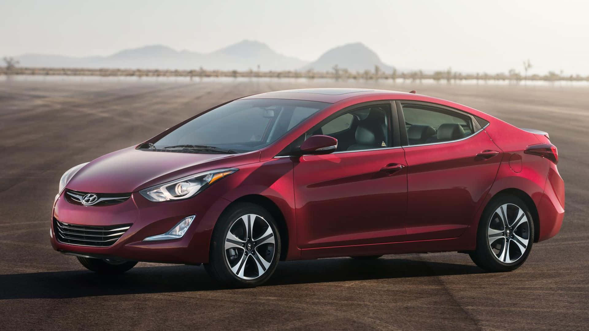 Hyundai Elantra 桌布 壁紙 — 一輛亮紅色現代Elantra房車停放在廣闊的沙漠道路上，遠山在朦朧的天空下。