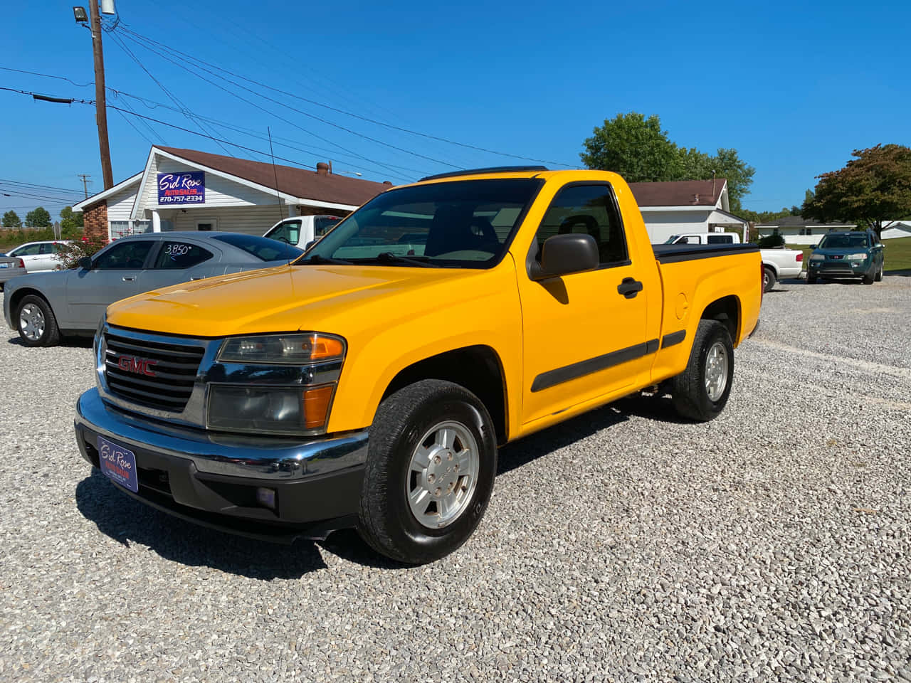 Gmc Canyon 桌布 壁紙 — 一輛亮黃色GMC皮卡車停在經銷商前的碎石地上，天空清澈湛藍。