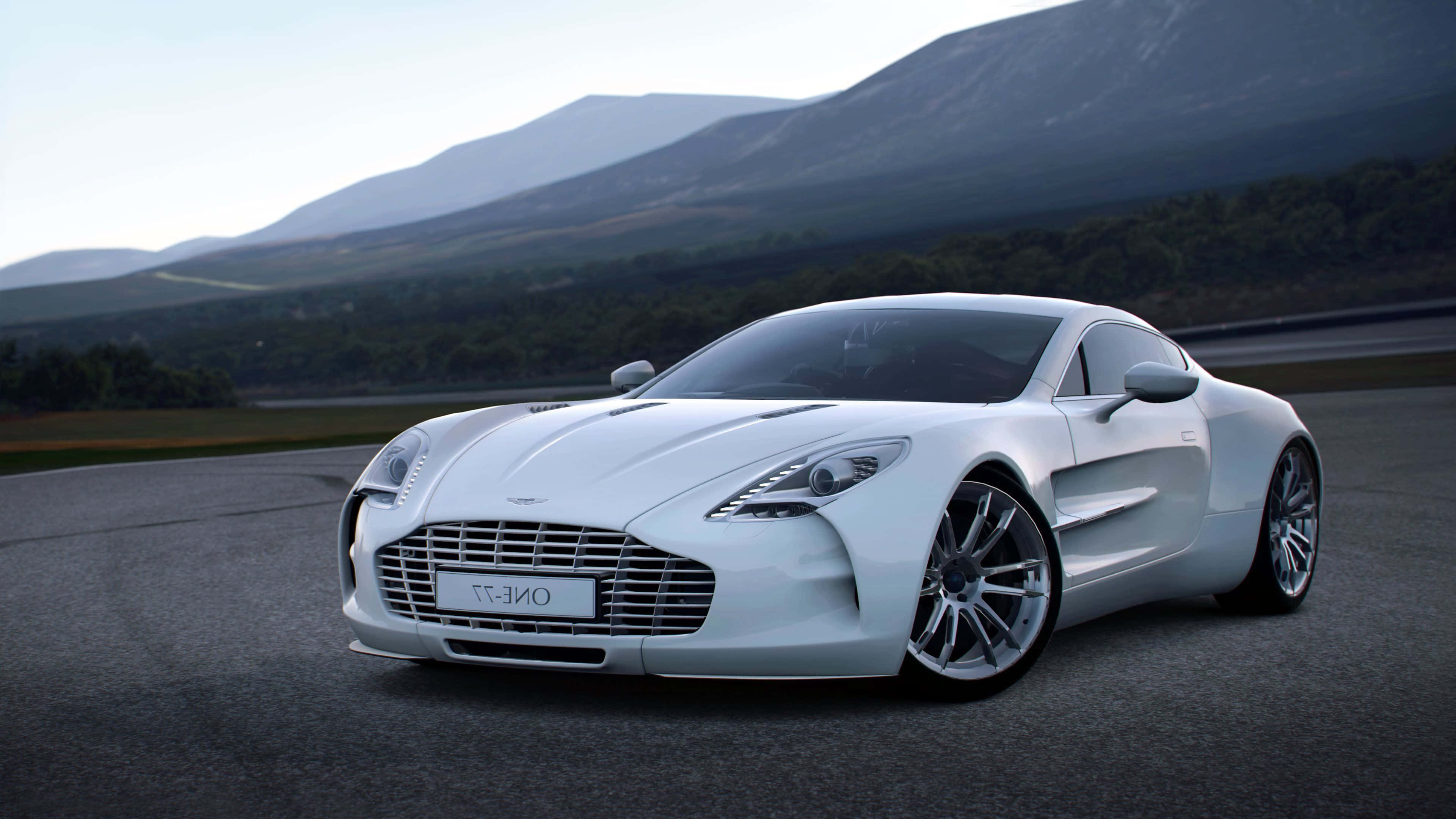 Aston Martin One-77 桌布 壁紙 — 一輛流線型白色Aston Martin One-77跑車在柔和日光下沿著蜿蜒的山路滑行。