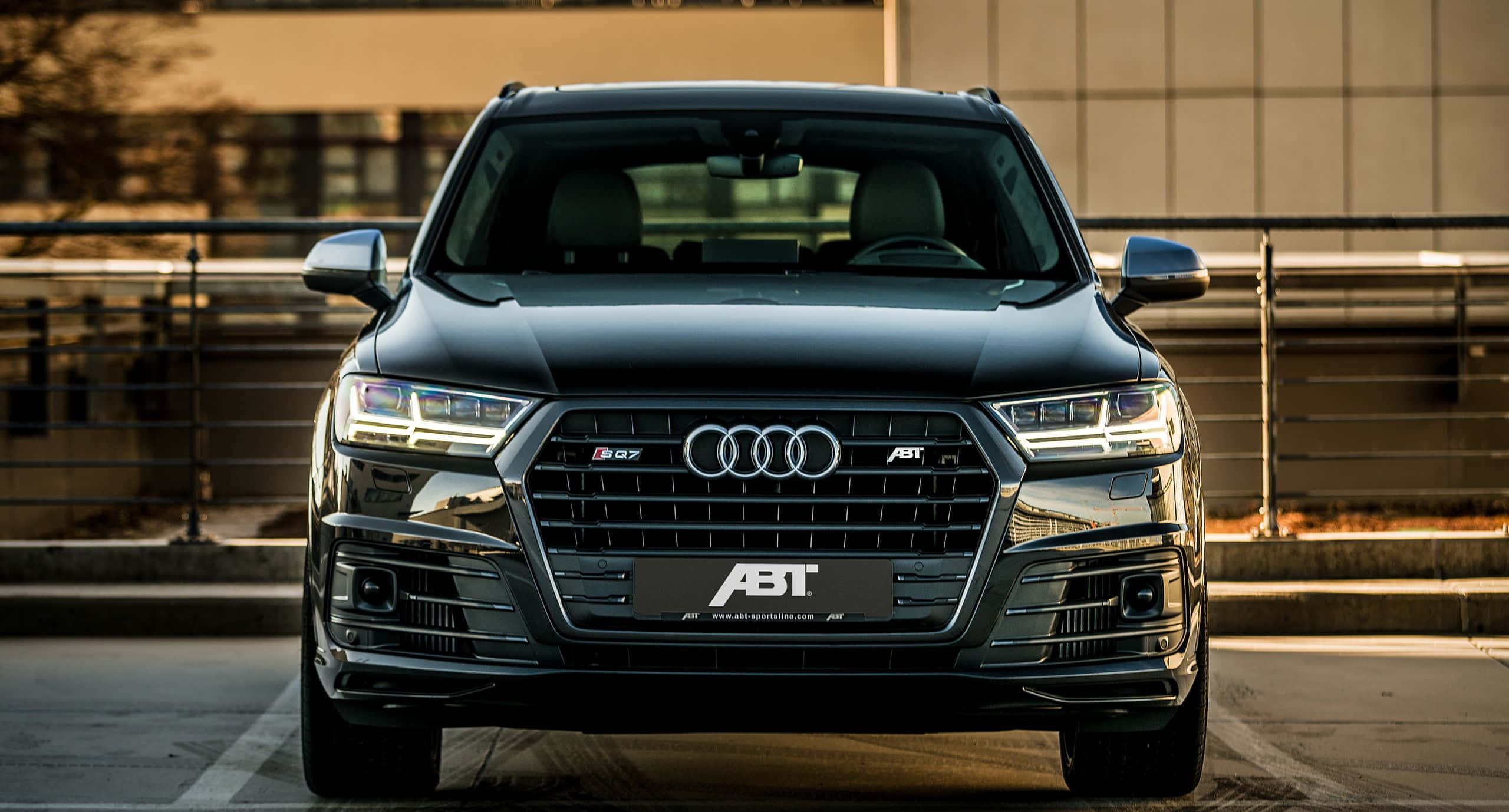 Audi Q7 桌布 壁紙 — 一輛流線型黑色ABT改裝奧迪SQ7 SUV，在溫暖的金色時刻光線下，配備銳利頭燈和鍍鉻飾件，正面朝前。