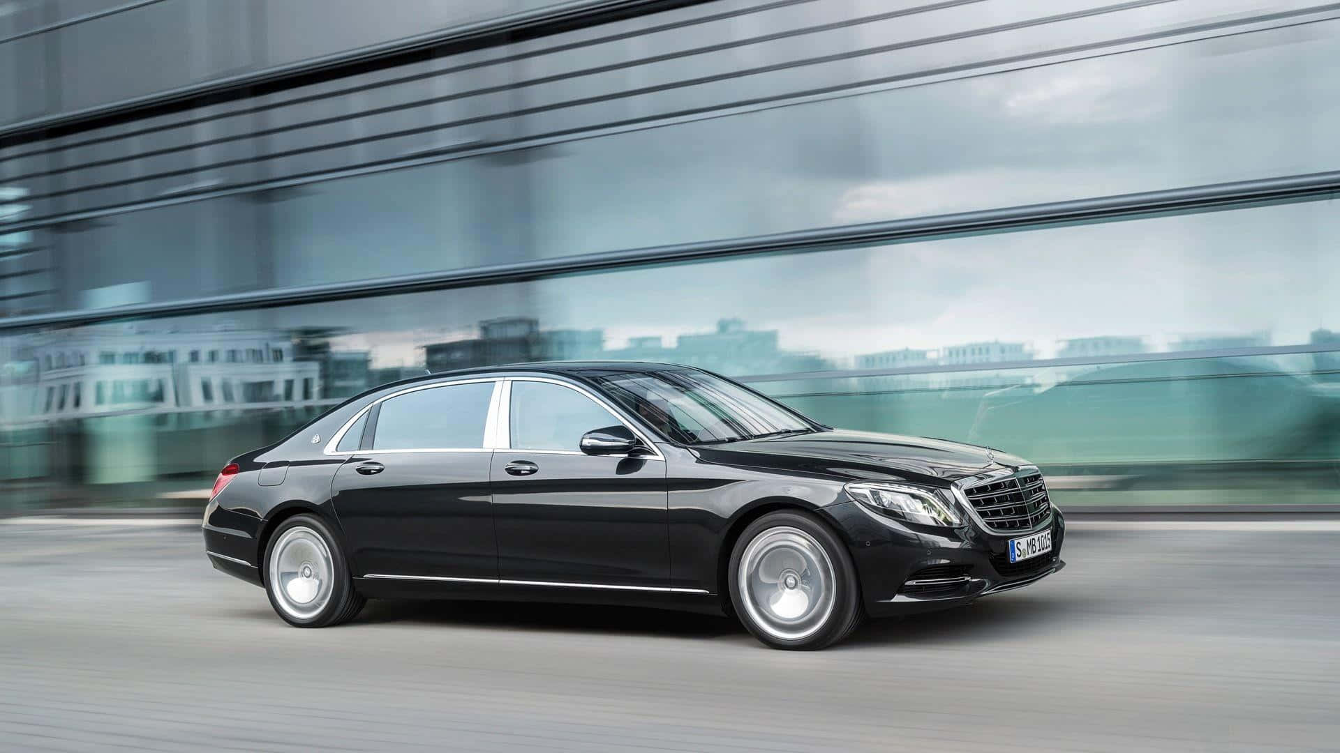 Maybach 桌布 壁紙 — 一輛流線型黑色賓士S-Class轎車在現代都市環境中快速滑行，背景是模糊的玻璃建築。