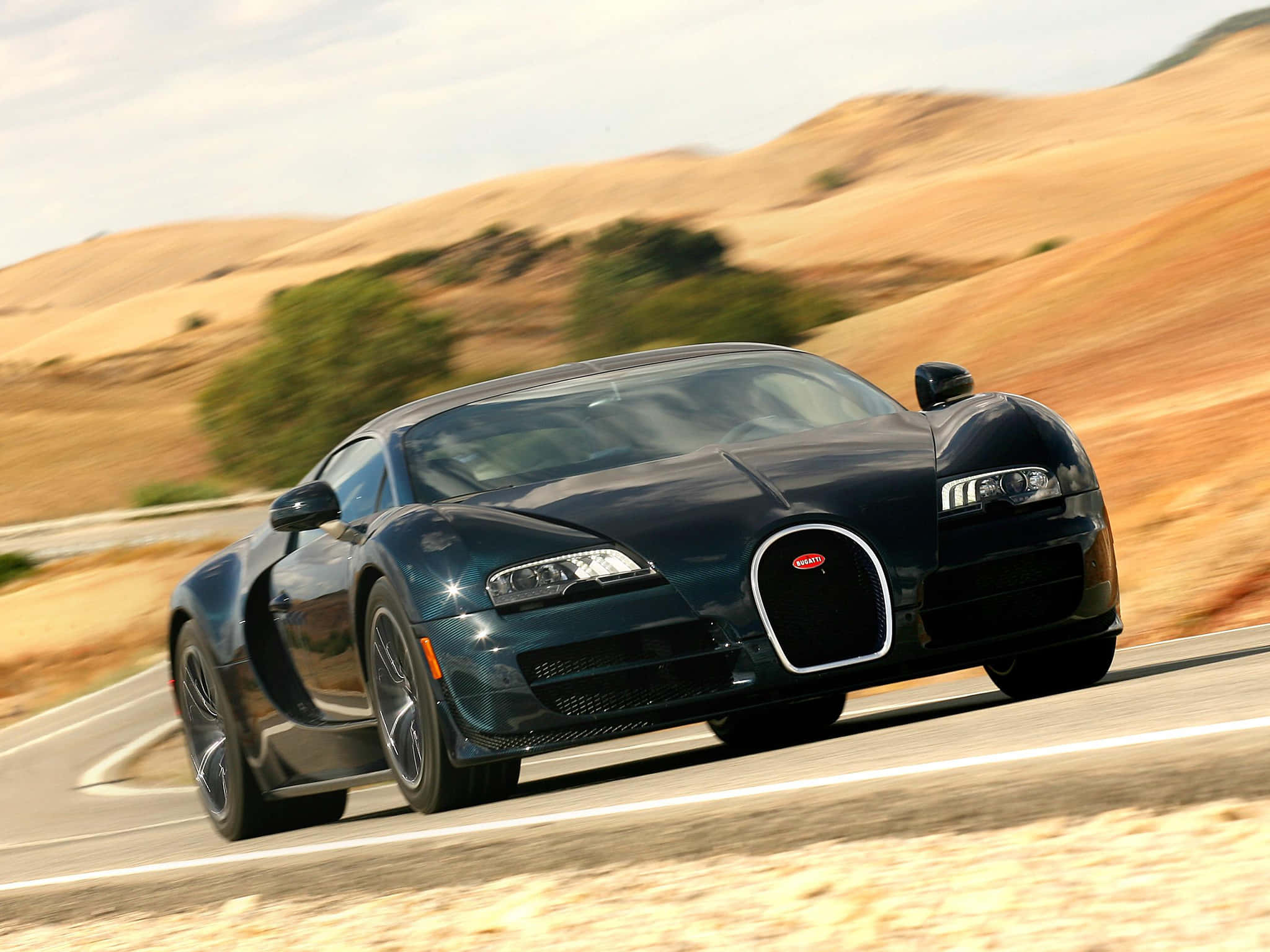 Bugatti Veyron 桌布 壁紙 — 一輛流線型黑色Bugatti Veyron在蜿蜒的沙漠公路上疾馳，背景是模糊的金色山丘。