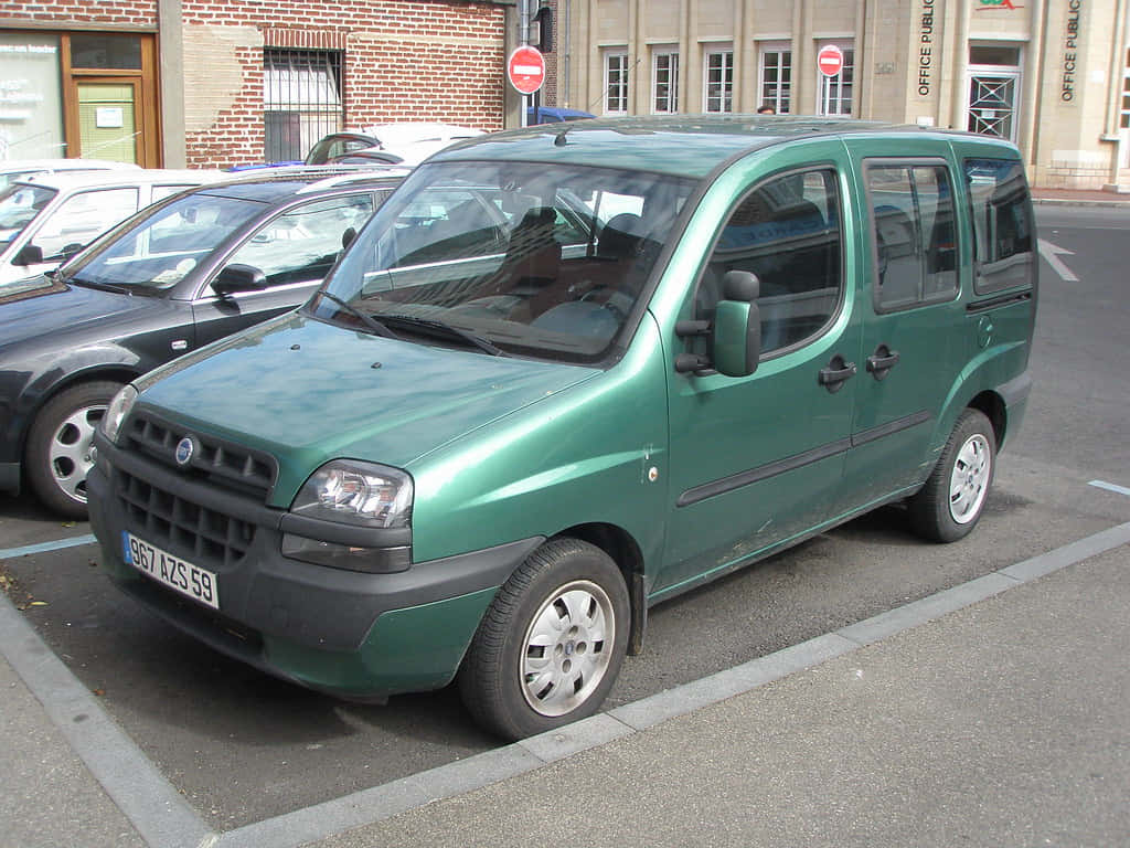  壁紙 — 一輛綠色Fiat Multipla小型貨車停放在城市地塊，附近有磚造建築和其他汽車。