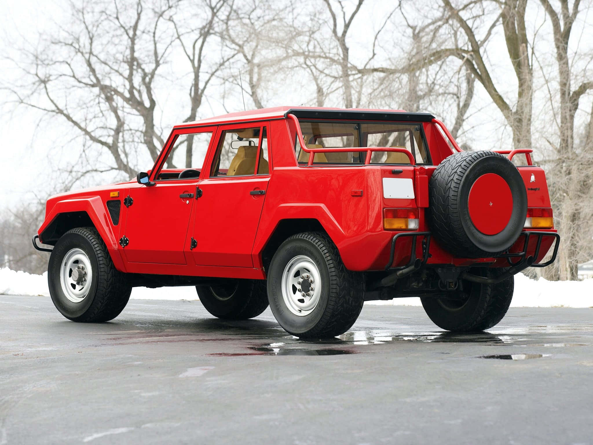 Lamborghini Lm002 桌布 壁紙 — 一輛搶眼的紅色藍寶堅尼LM002停泊在濕漉漉的路面上，周圍是灑滿白雪的禿樹。