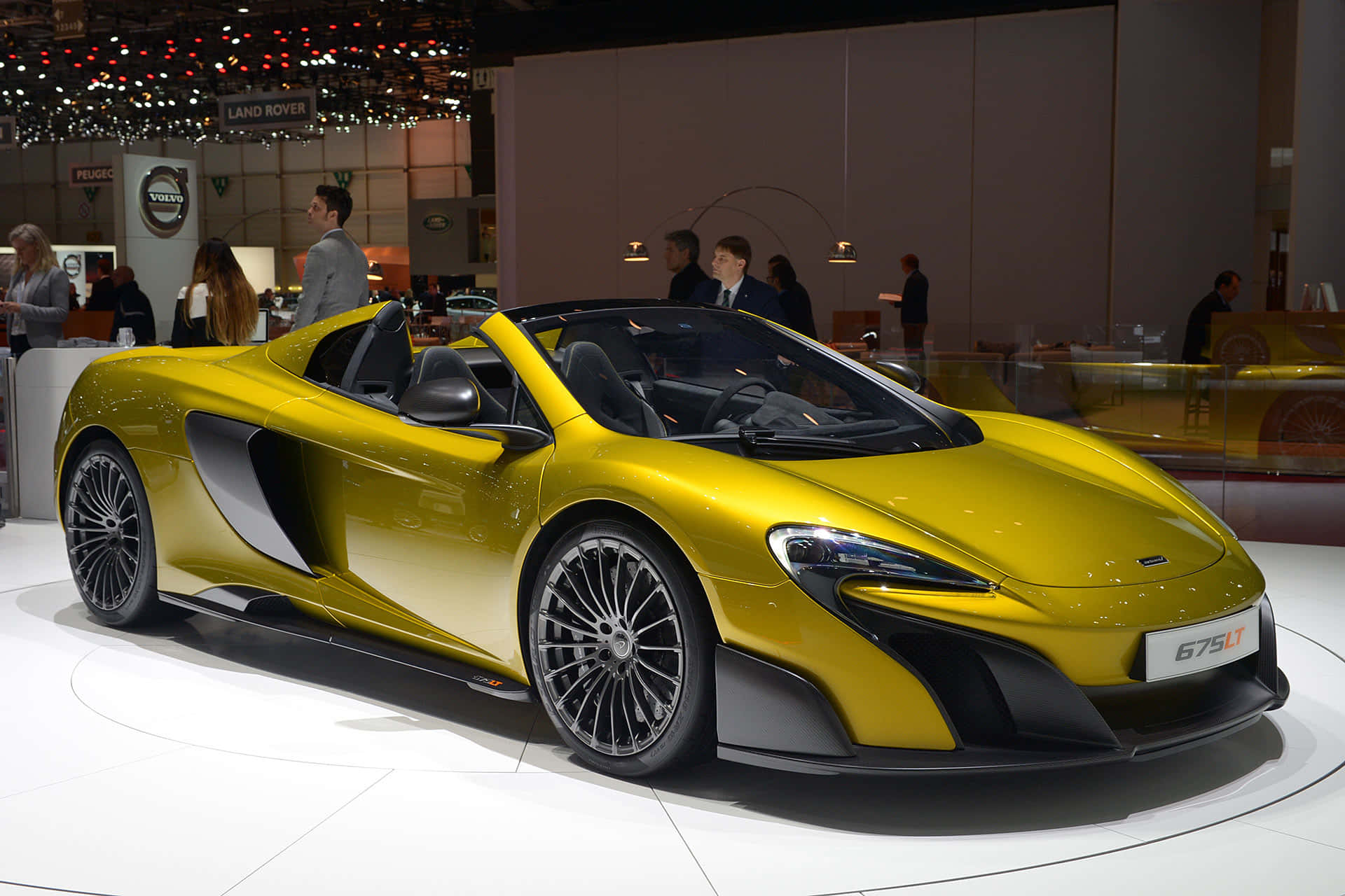 Mclaren 675lt Spider 桌布 壁紙 — 一輛閃亮的黃色McLaren 675LT Spider在車展上展出，拋光的曲線和黑色飾邊在明亮的燈光下熠熠生輝。