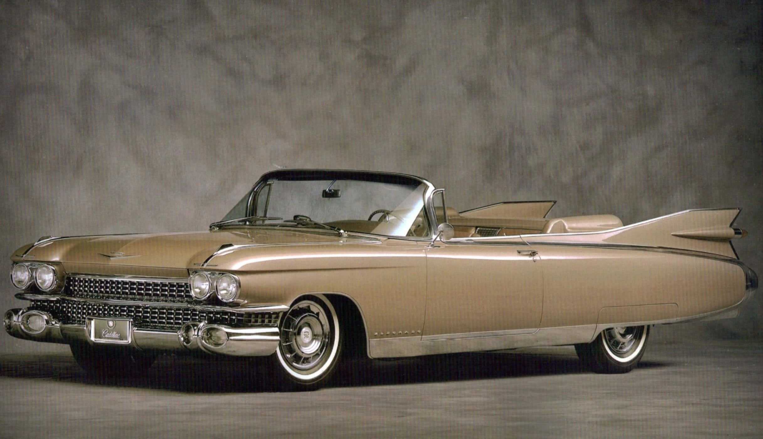 Cadillac Eldorado 桌布 壁紙 — 一輛閃亮的金色1959年凱迪拉克敞篷車，帶有尾鰭和鍍鉻細節，擺放在質感灰色工作室背景前。