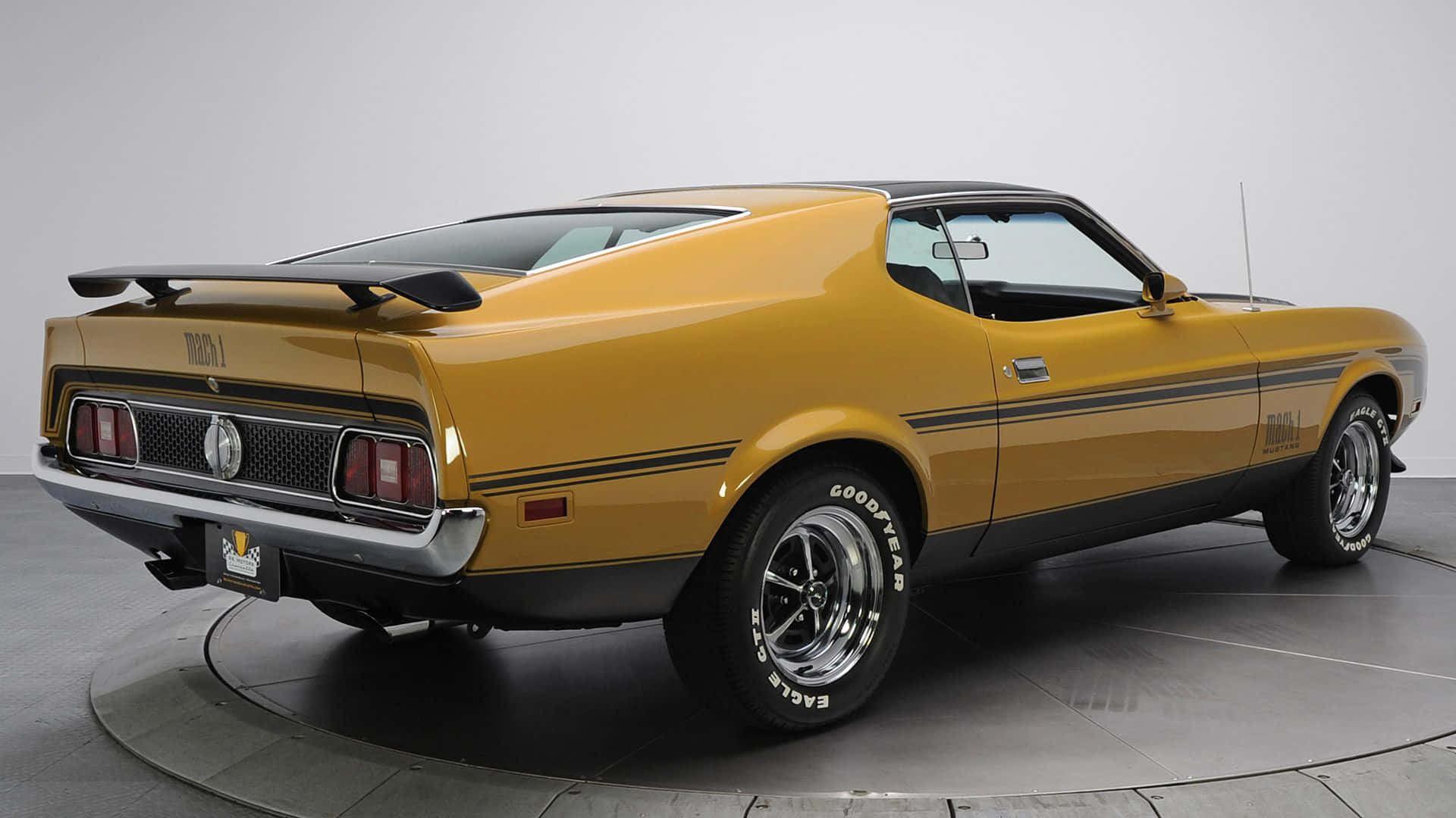 Ford Mustang Mach 1 桌布 壁紙 — 一輛閃亮的金色1970年代福特野馬Mach 1，帶有黑色賽車條紋和鍍鉻輪圈，在簡約的攝影棚環境中展示。