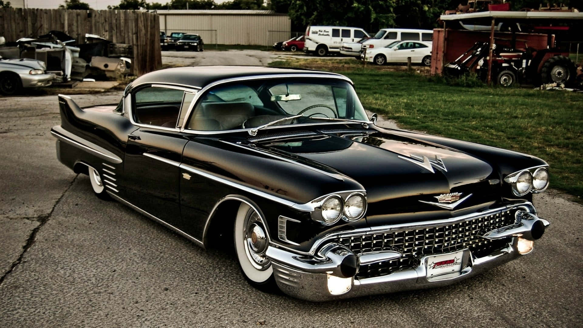Cadillac Eldorado 桌布 壁紙 — 一輛閃亮黑色1959年凱迪拉克，帶有鍍鉻裝飾和白色輪胎，停在鄉村庭院破裂的瀝青上。