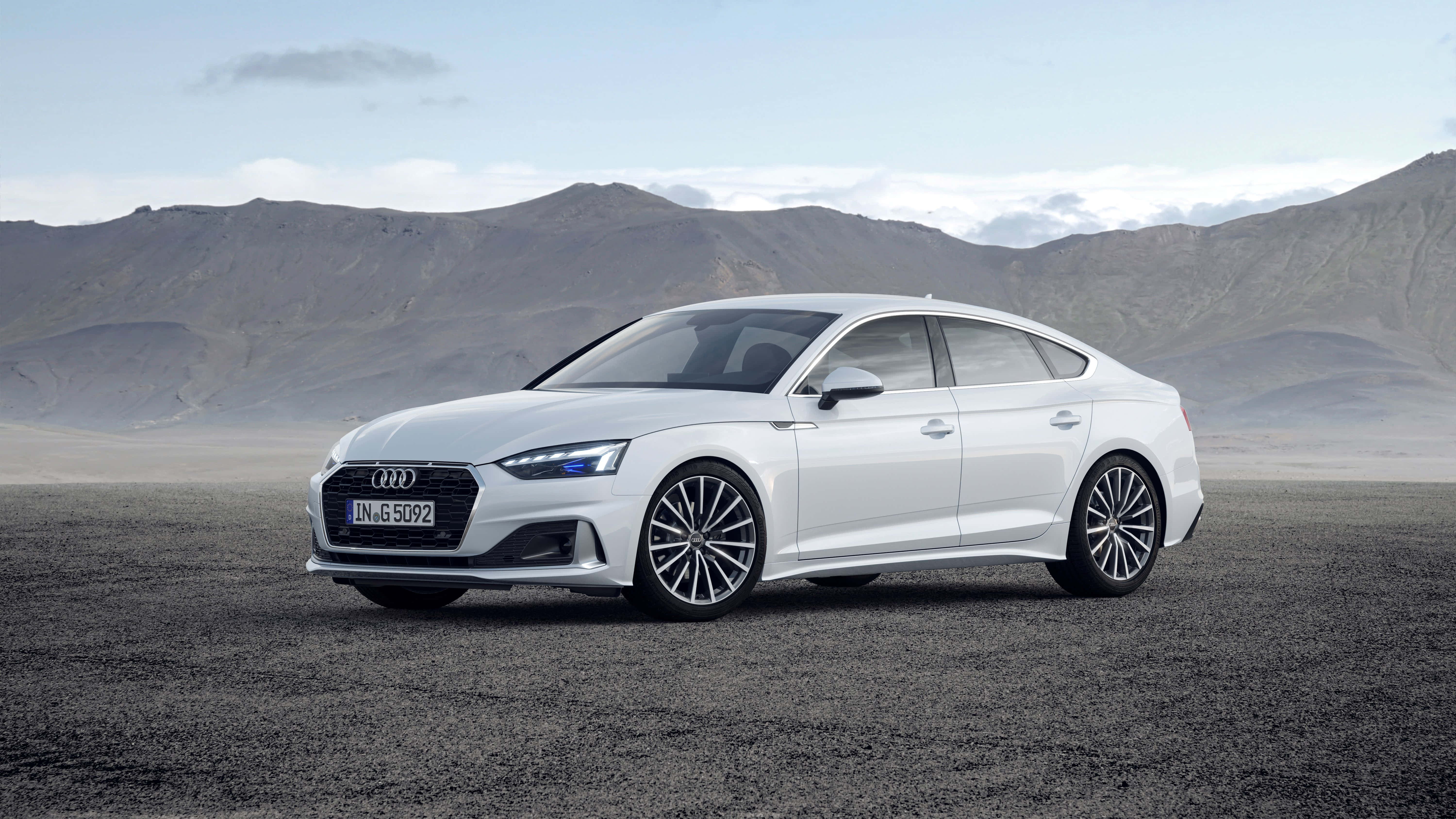 Audi A5 桌布 壁紙 — 一輛時尚的白色Audi轎車停泊在碎石平原上，背景是蒼白天空下的崎嶇山脈。