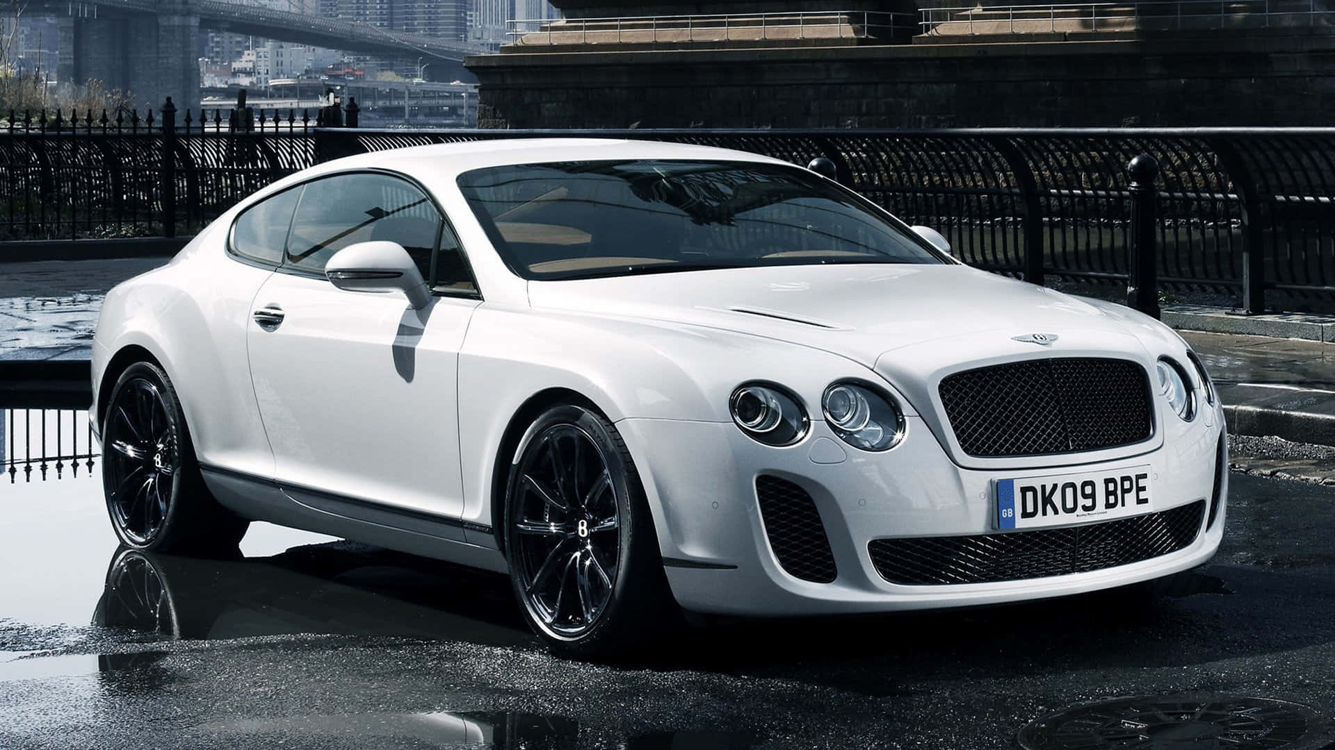 Bentley Continental Supersports 桌布 壁紙 — 一輛時尚的白色賓利 Continental GT 雙門轎跑車，在城市的燈光下，以橋樑為背景，在潮濕的路面上閃閃發光。