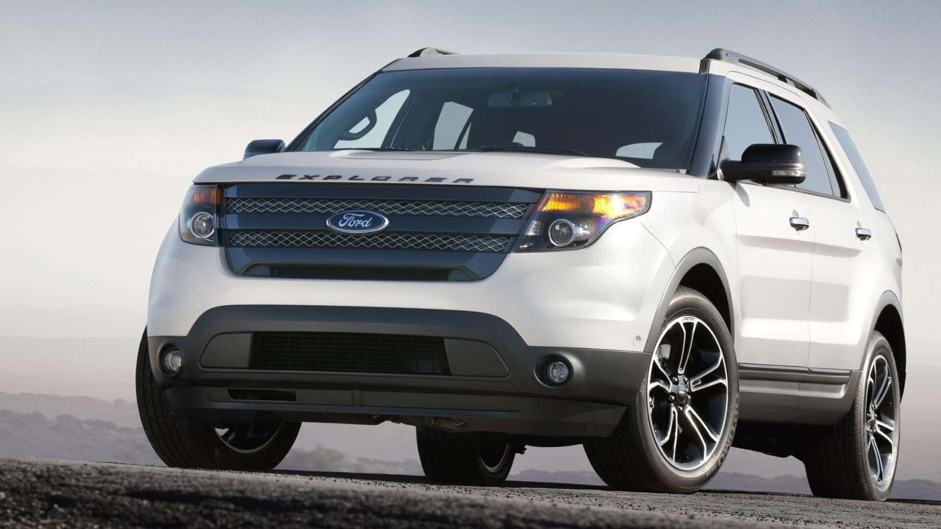 Ford Edge 桌布 壁紙 — 一輛時尚的白色福特 Explorer SUV 停泊在鋪砌道路上，背景是朦朧的山脈，天空明亮。