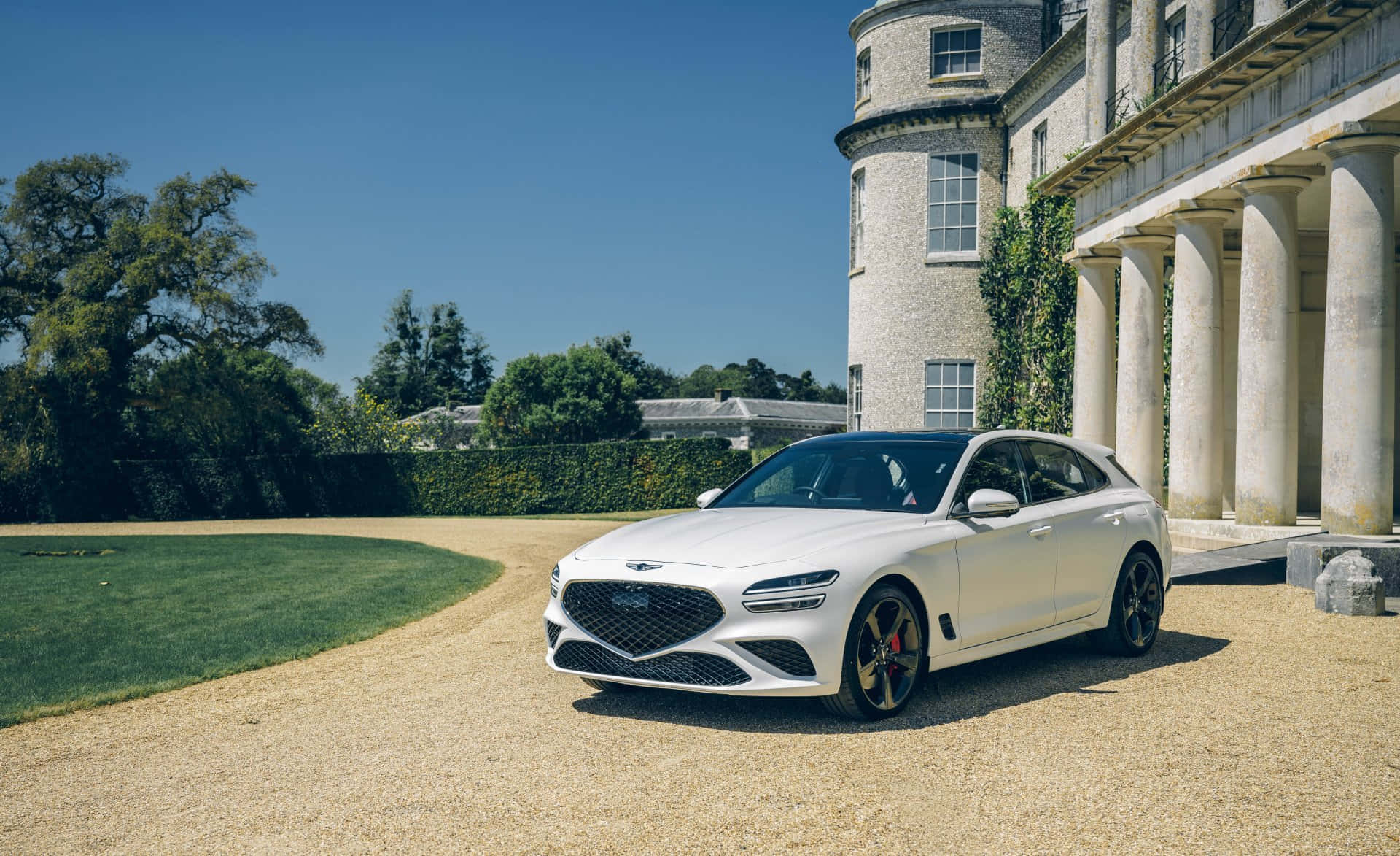 Genesis G70 桌布 壁紙 — 一輛時尚的白色豪華SUV停泊在碎石路上，前方是一座宏偉的石砌豪宅，有柱子和常春藤，天空清澈湛藍。
