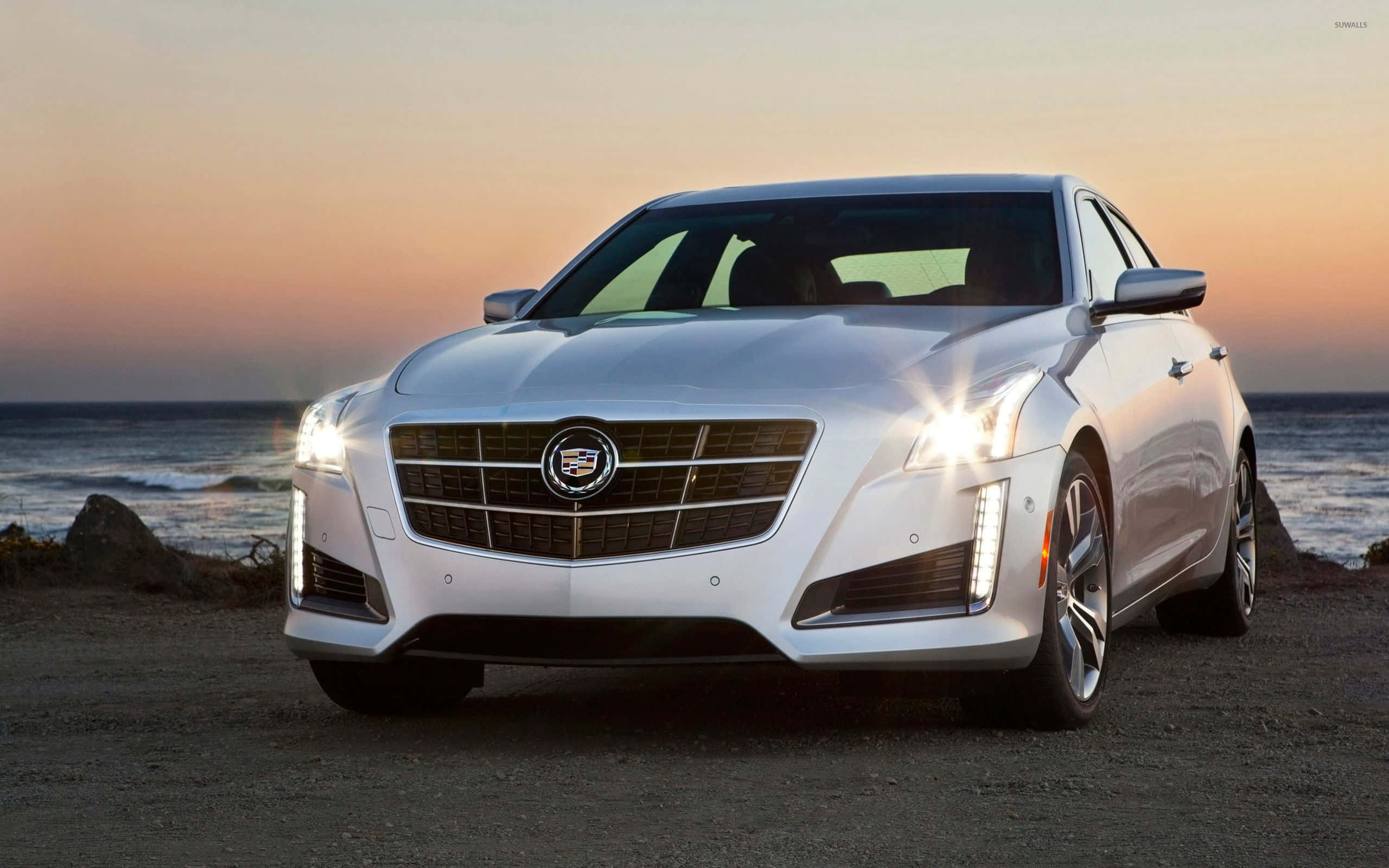 Cadillac Cts 桌布 壁紙 — 一輛時尚的白色凱迪拉克CT6轎車閃耀著車頭燈，停在日落時分的岩石海灘上，背後有海浪拍打。