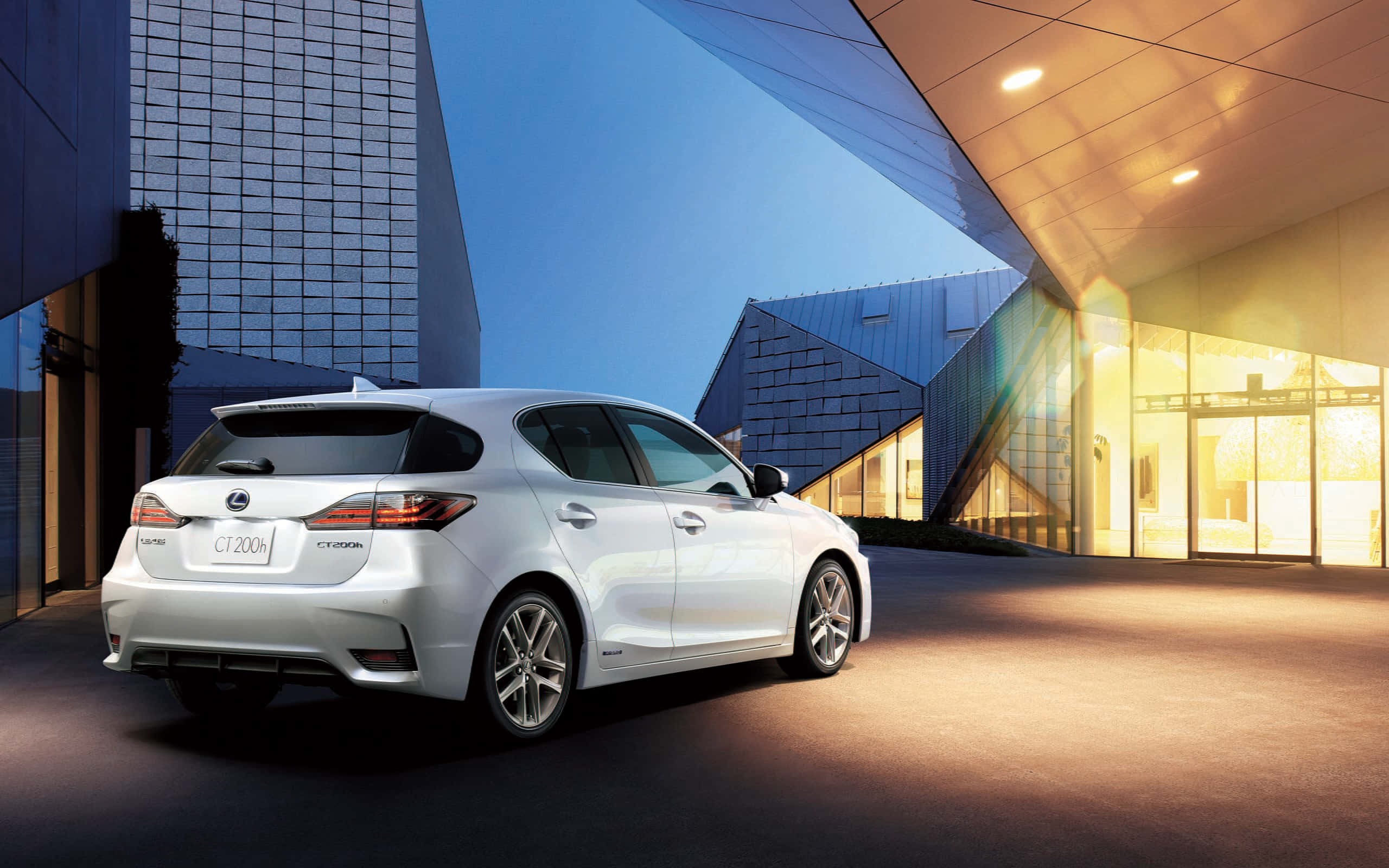 Lexus Ct 200h 桌布 壁紙 — 一輛時尚的白色Lexus CT 200h在黃昏時停在一棟現代玻璃建築外，建築內有溫暖的燈光。
