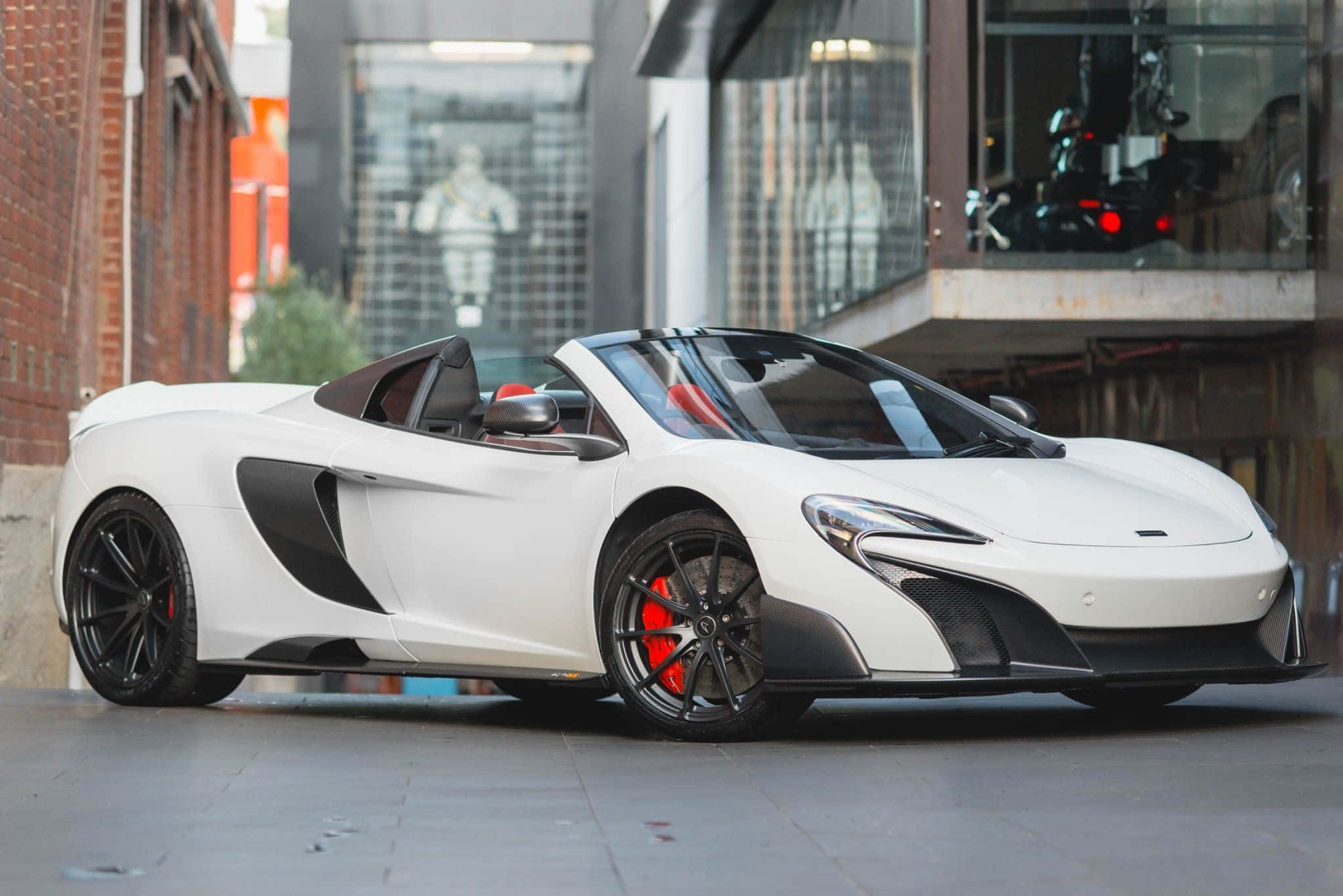 Mclaren 675lt Spider 桌布 壁紙 — 一輛時尚的白色McLaren跑車，帶有黑色飾邊和紅色制動卡鉗，停在城市人行道上，靠近磚砌建築。