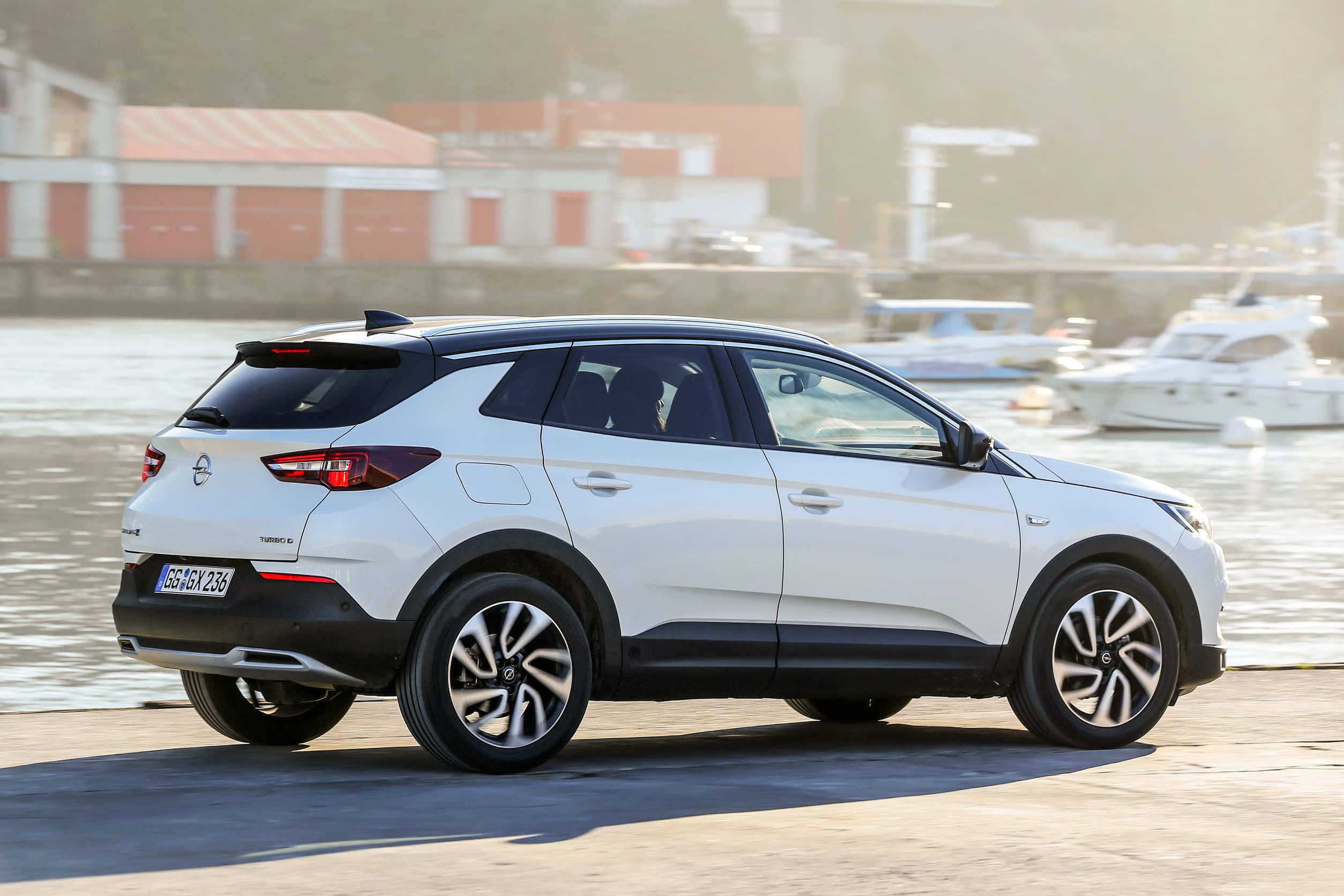 Opel Grandland X 桌布 壁紙 — 一輛時尚的白色SUV停泊在港口，背景有船隻和紅色建築物，略顯朦朧。