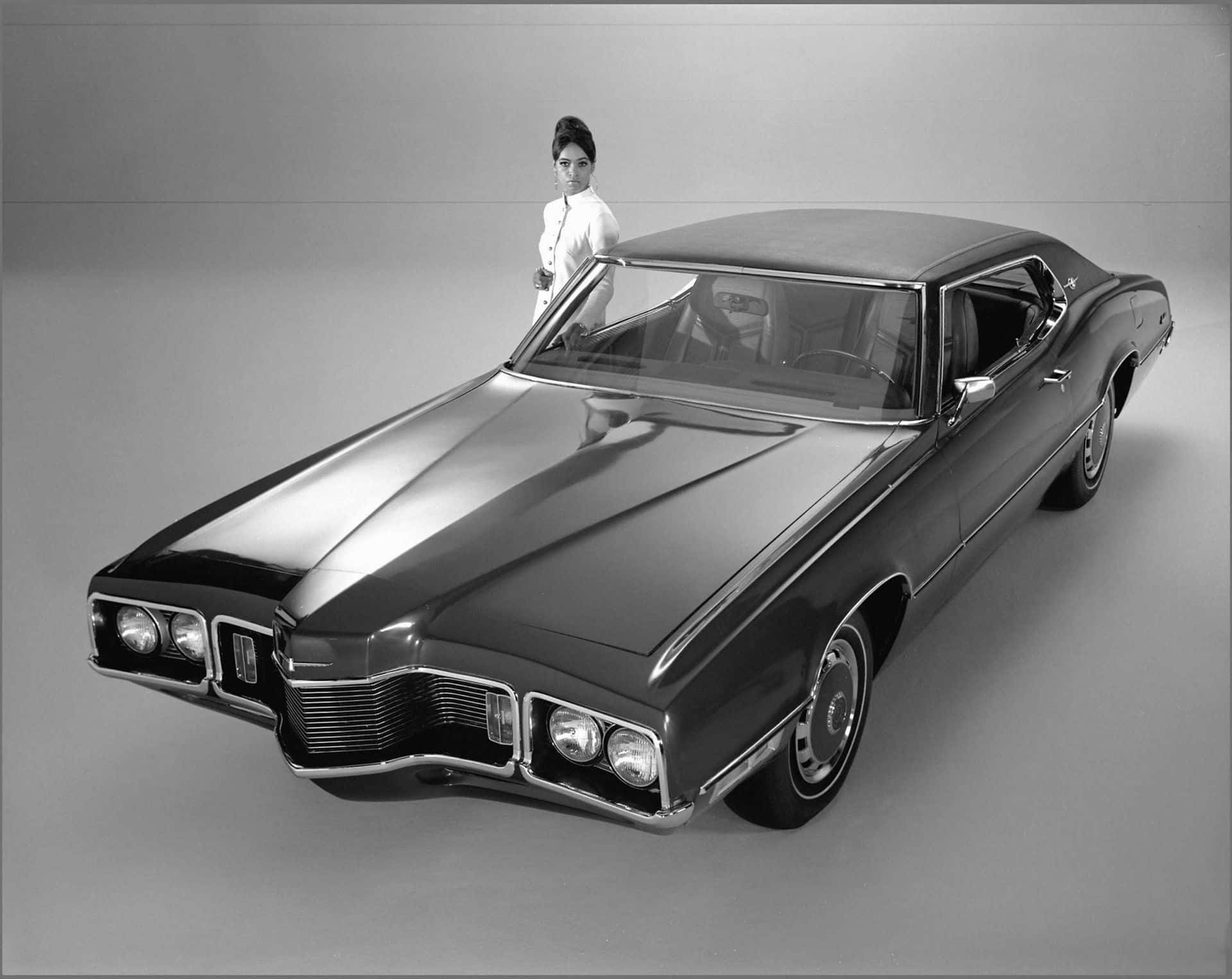 Ford Thunderbird 桌布 壁紙 — 一輛時尚的復古肌肉車在攝影棚燈光下閃閃發光，一位優雅的女士靠在駕駛座車門上。