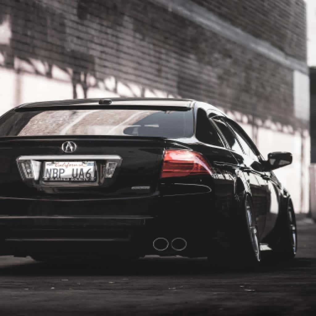 Acura Tl 桌布 壁紙 — 一輛時尚的黑色Acura轎車，紅色尾燈發光，停泊在都市陰影中風化的磚牆旁。