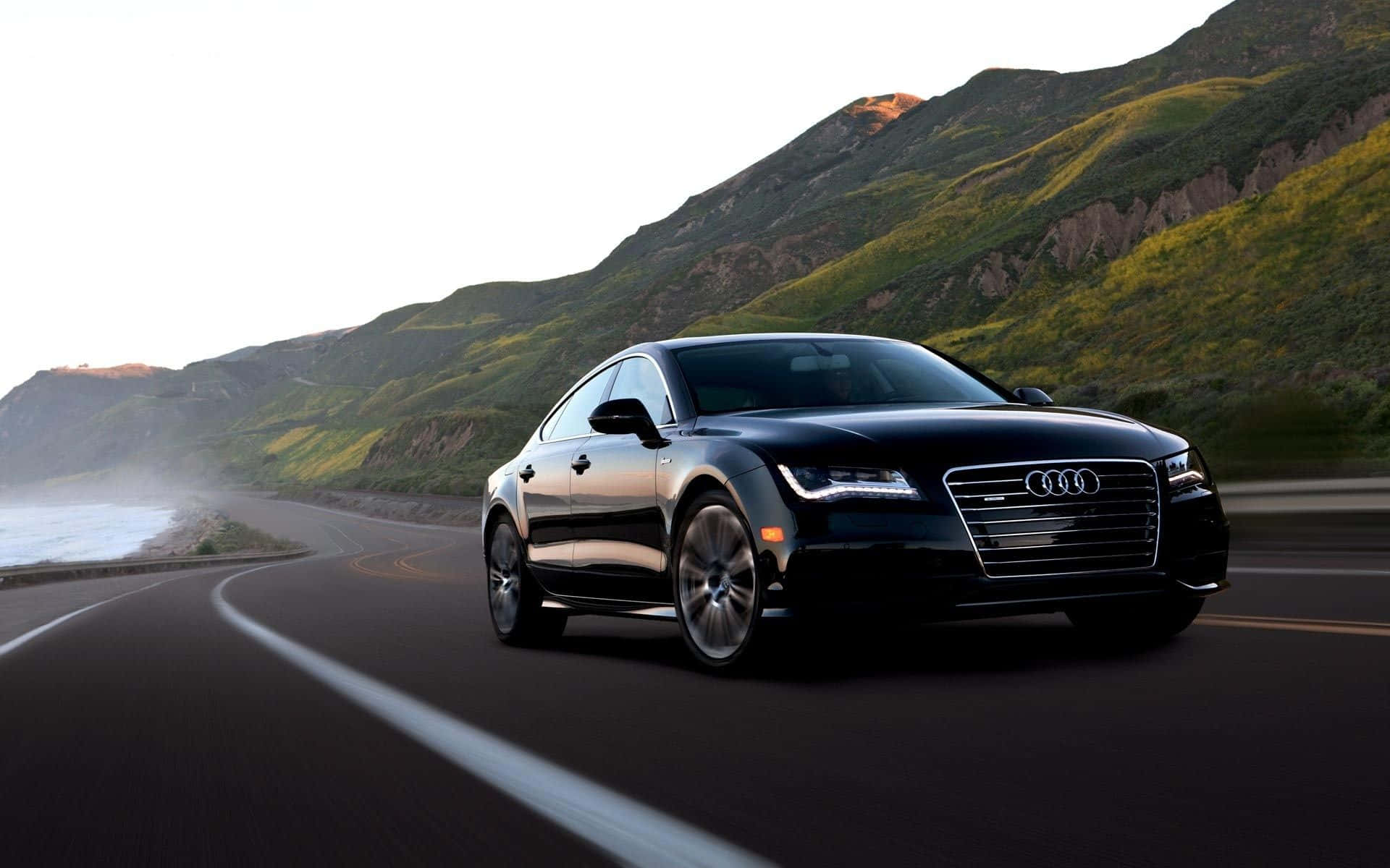 Audi S6 桌布 壁紙 — 一輛時尚的黑色奧迪轎車沿著海岸公路行駛，背景是綠色山丘和海洋薄霧。