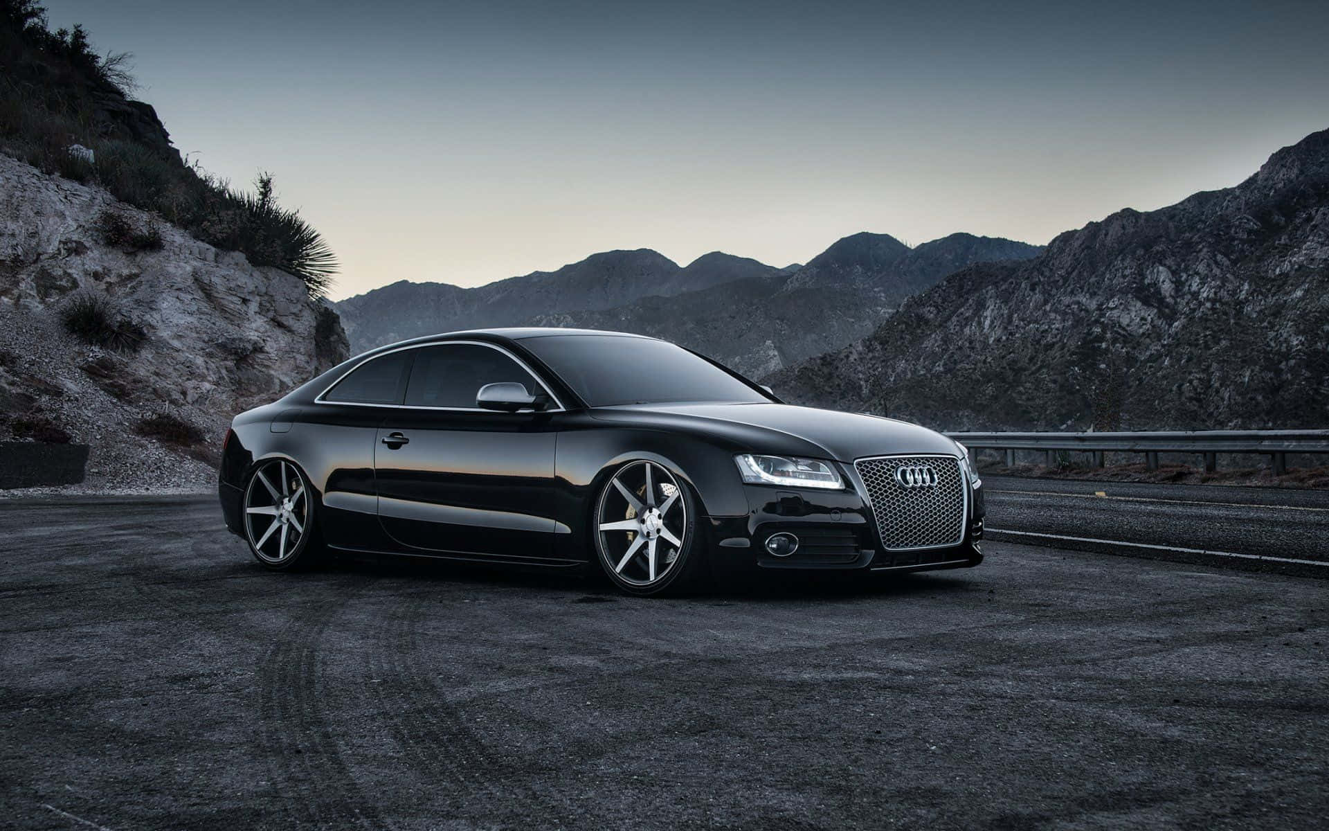 Audi S6 桌布 壁紙 — 一輛時尚的黑色奧迪轎跑車停泊在暮色中的山路上，背景是崎嶇的山峰。
