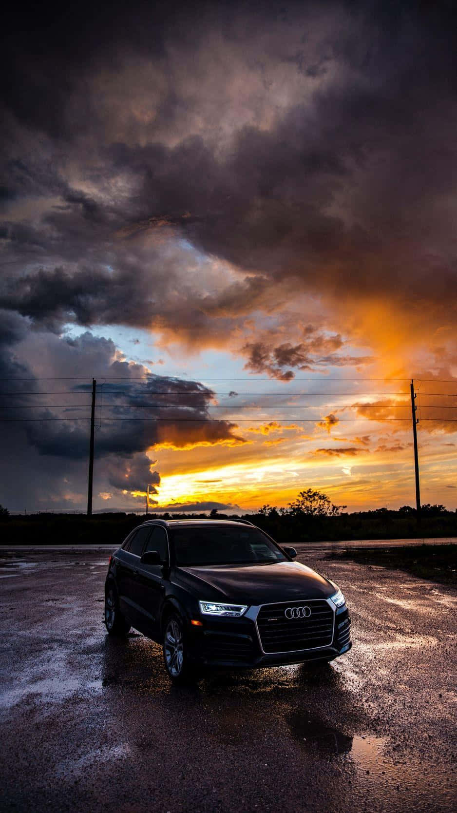 Audi Q5 桌布 壁紙 — 一輛時尚的黑色Audi SUV停泊在濕漉漉的瀝青停車場上，頭頂是戲劇性的日落天空，有火橙色的雲和黑暗的風暴雲。