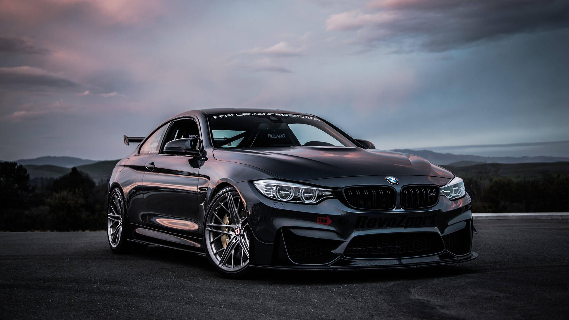 黑色BMW M4跑車在黃昏時停在路上，後面有山丘 — 汽車 壁紙