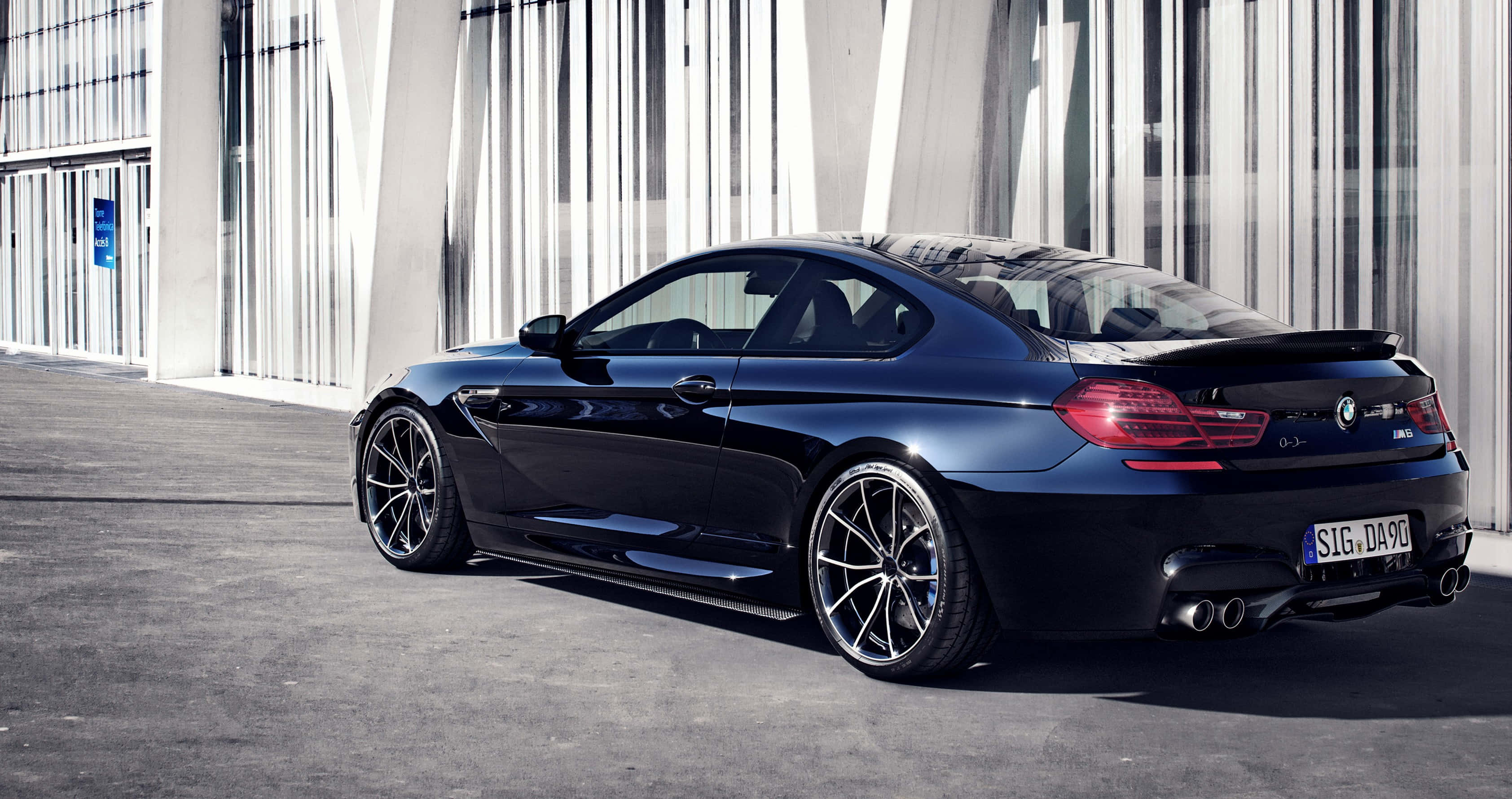 Bmw M6 桌布 壁紙 — 一輛時尚的黑色BMW M6雙門轎跑車停在一棟現代玻璃和鋼結構建築前，在明亮的日光下。