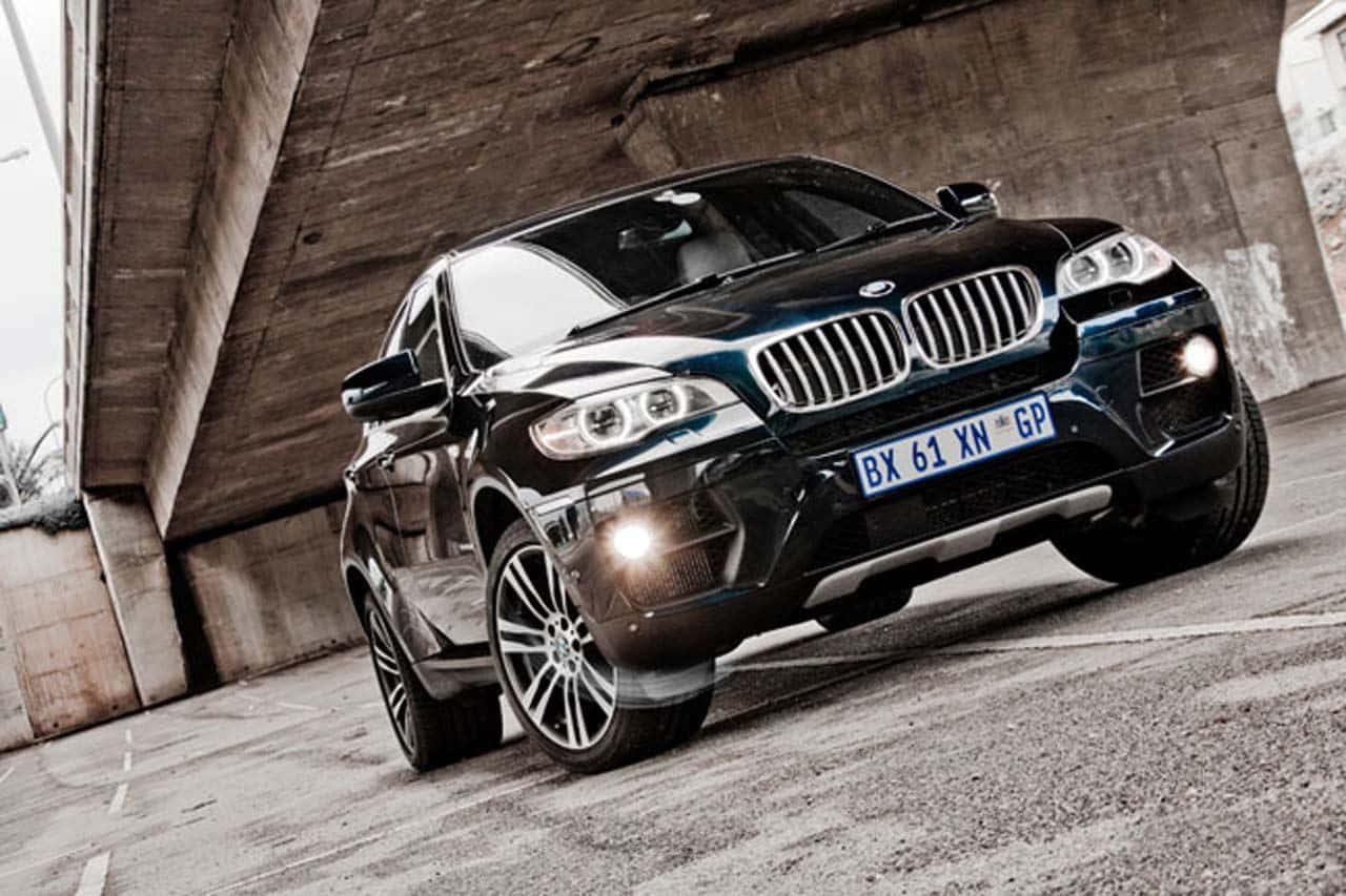 Bmw X6 桌布 壁紙 — 一輛時尚的黑色BMW X6 SUV在惡劣光線下，於風化的混凝土天橋下閃閃發光。