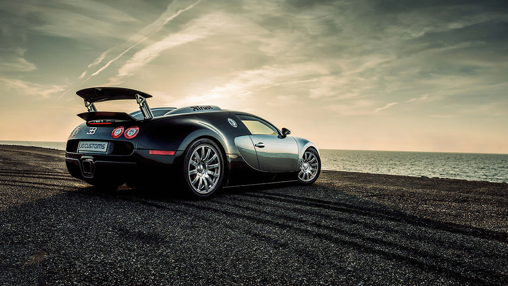 Bugatti Veyron 桌布 壁紙 — 一輛時尚的黑色Bugatti Veyron停泊在日落時分的礫石海灘上，背景有海浪。