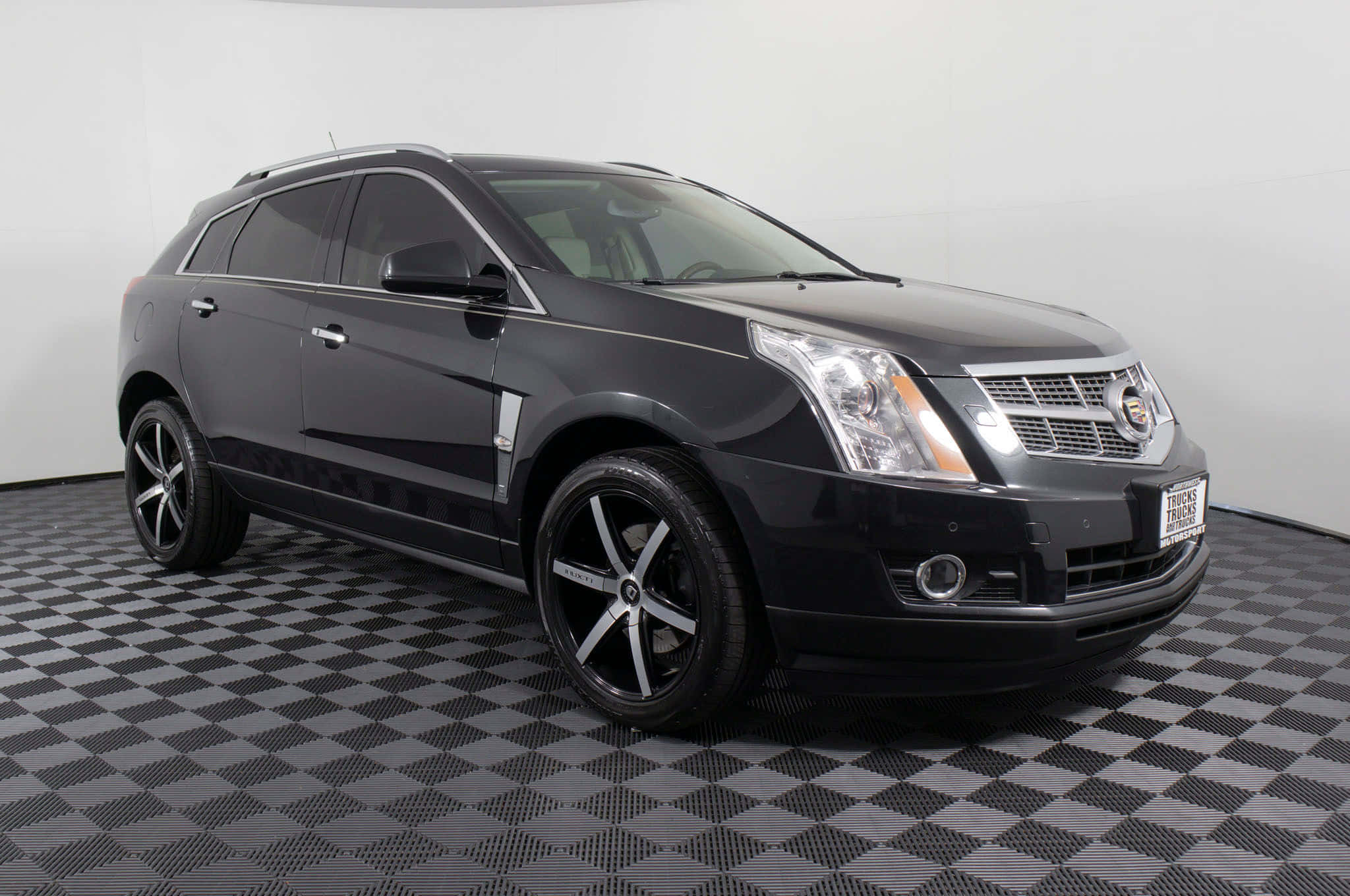 Cadillac Srx 桌布 壁紙 — 一輛時尚的黑色Cadillac SRX SUV在工作室中展示，地板為棋盤格，牆壁為白色。