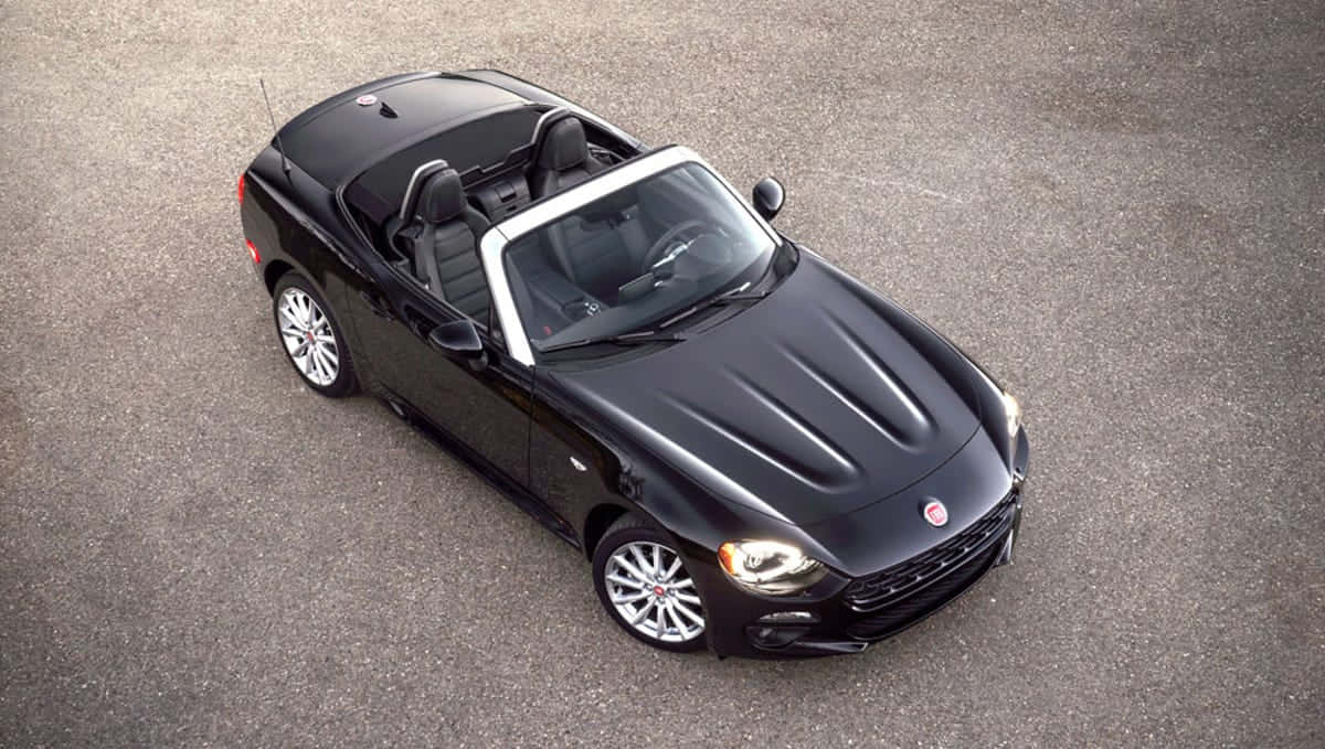 Fiat 124 Spider 桌布 壁紙 — 一輛時尚的黑色敞篷跑車，配有白色軟頂，停在灰色瀝青路面上。