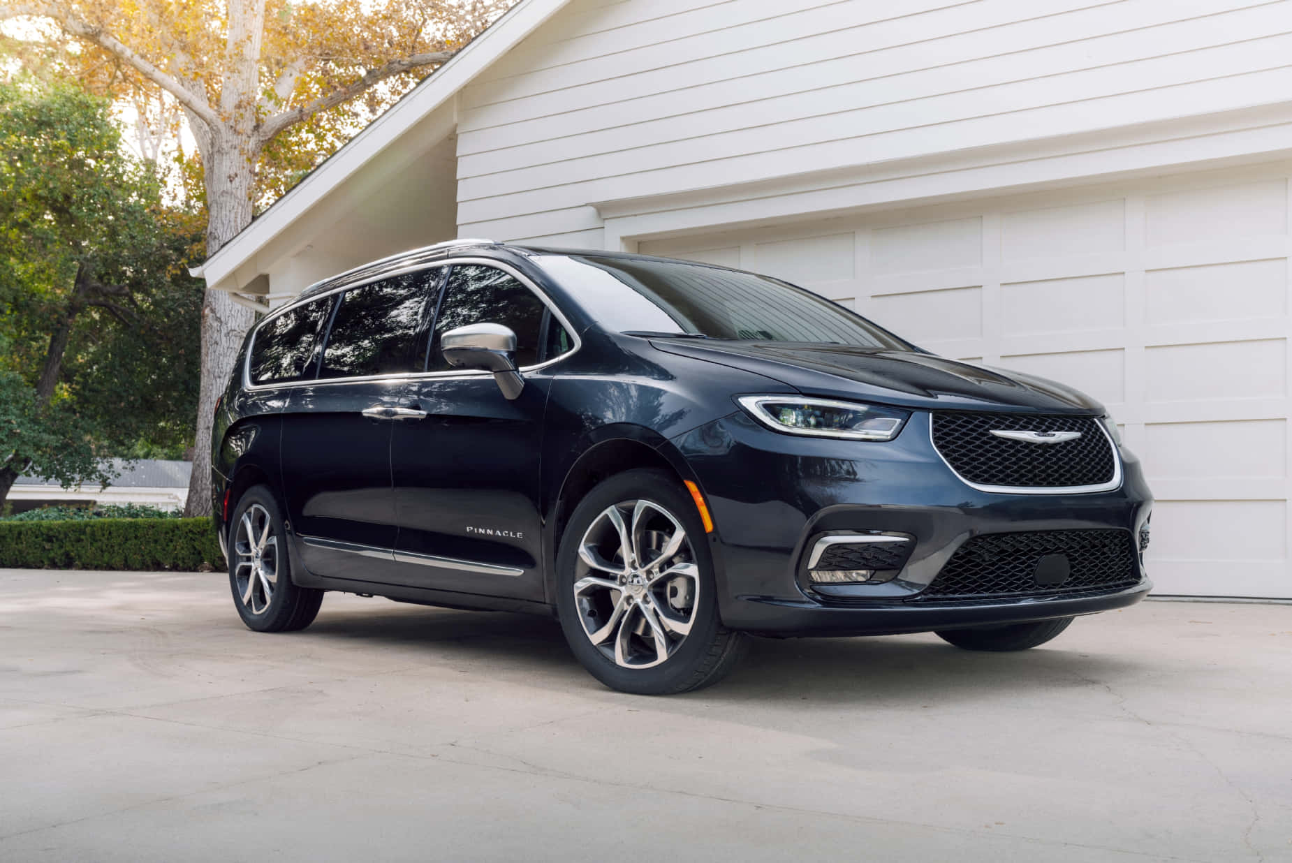 Chrysler Pacifica 桌布 壁紙 — 一輛時尚的黑色Chrysler Pacifica小型貨車停在白色車庫前，背景有樹木和柔和陽光。