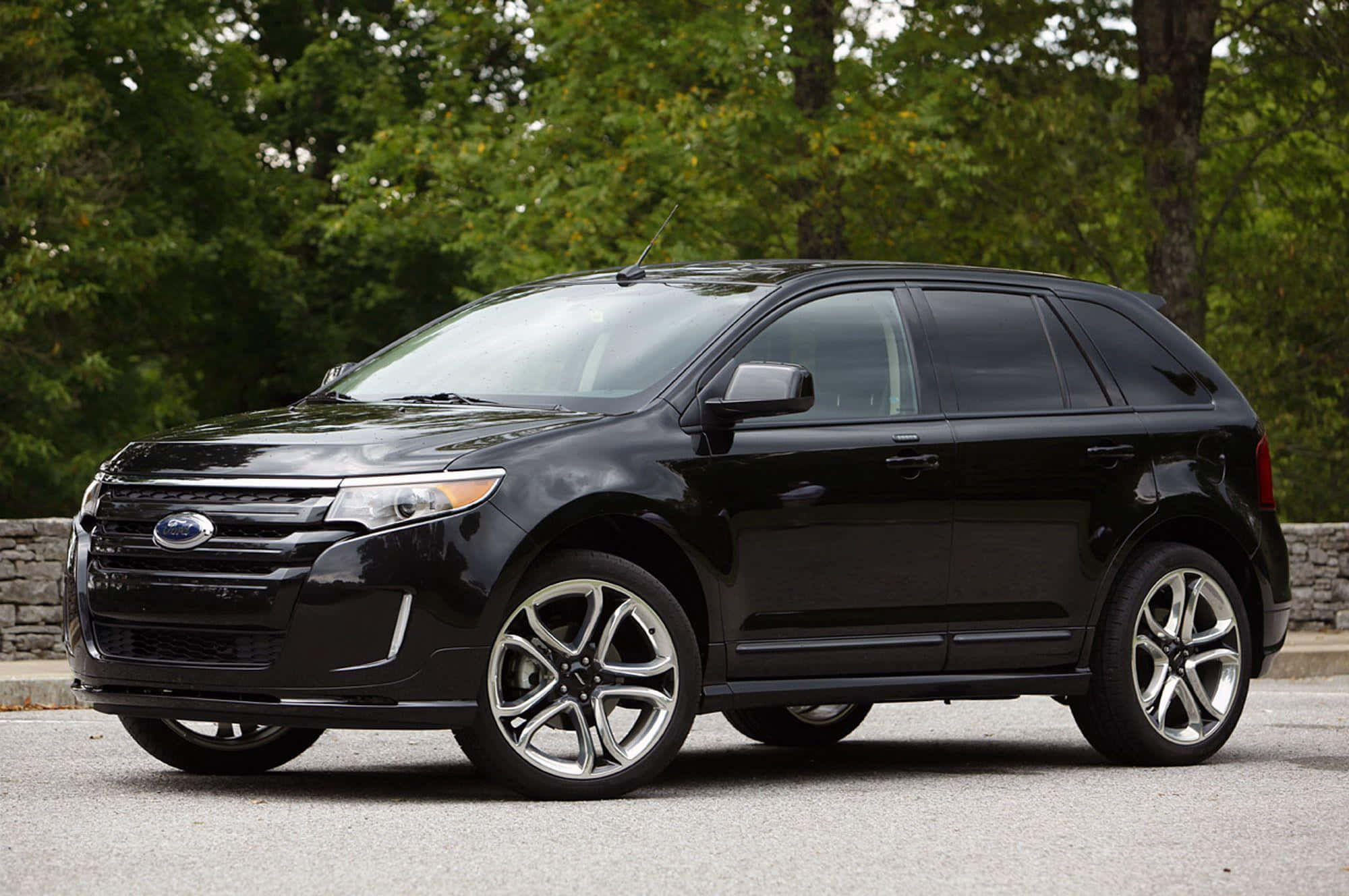 Ford Edge 桌布 壁紙 — 一輛時尚的黑色福特 Edge SUV 停在柏油路上，背景是茂密的綠色樹木。