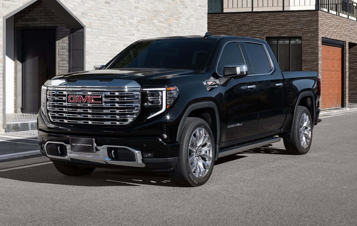Gmc Sierra 桌布 壁紙 — 一輛時尚的黑色GMC Sierra Denali皮卡車停在鋪砌的街道上，前面是現代磚砌建築，在明亮的日光下。